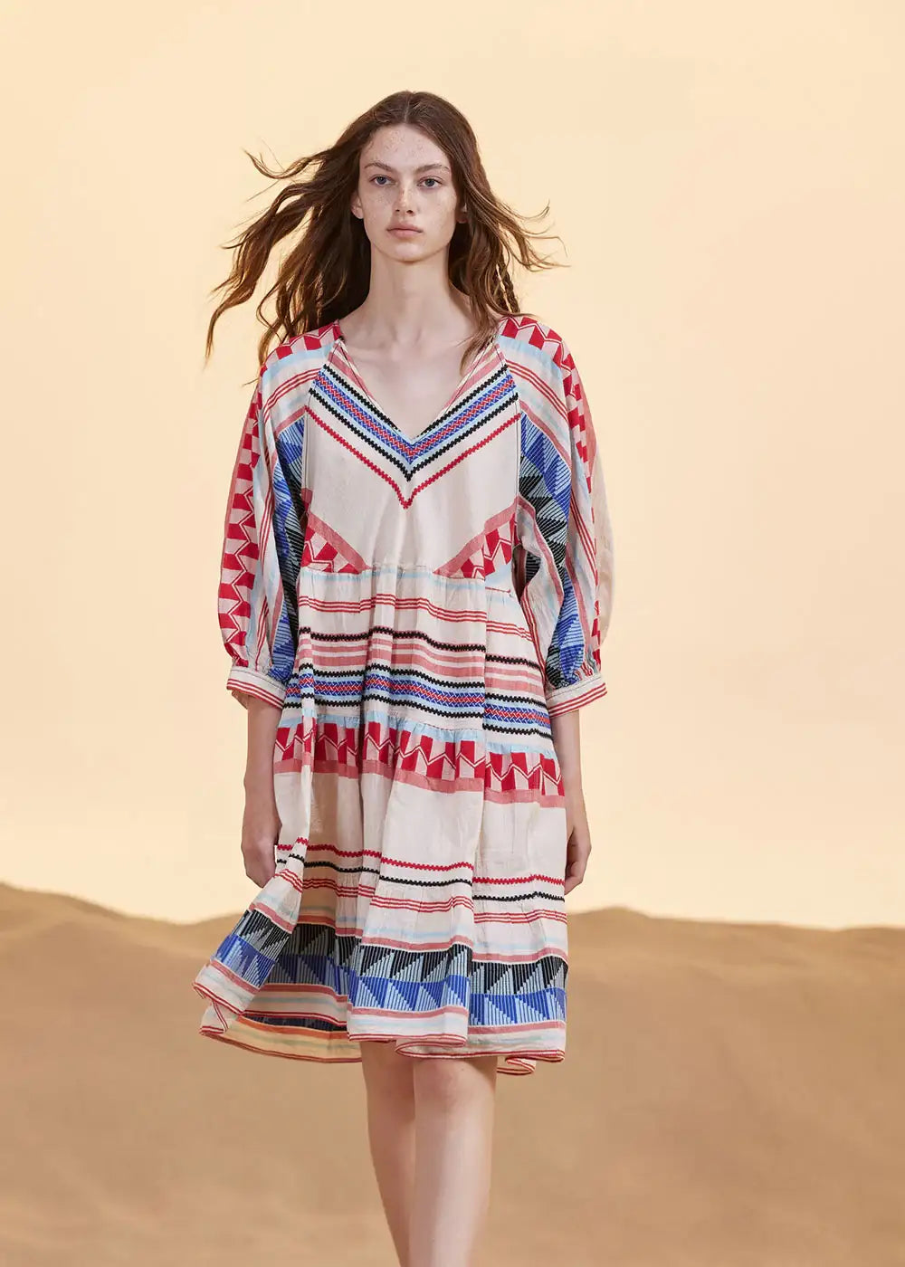 Woman wearing a patterned boho dress with red, blue, and geometric stripes in a desert setting
