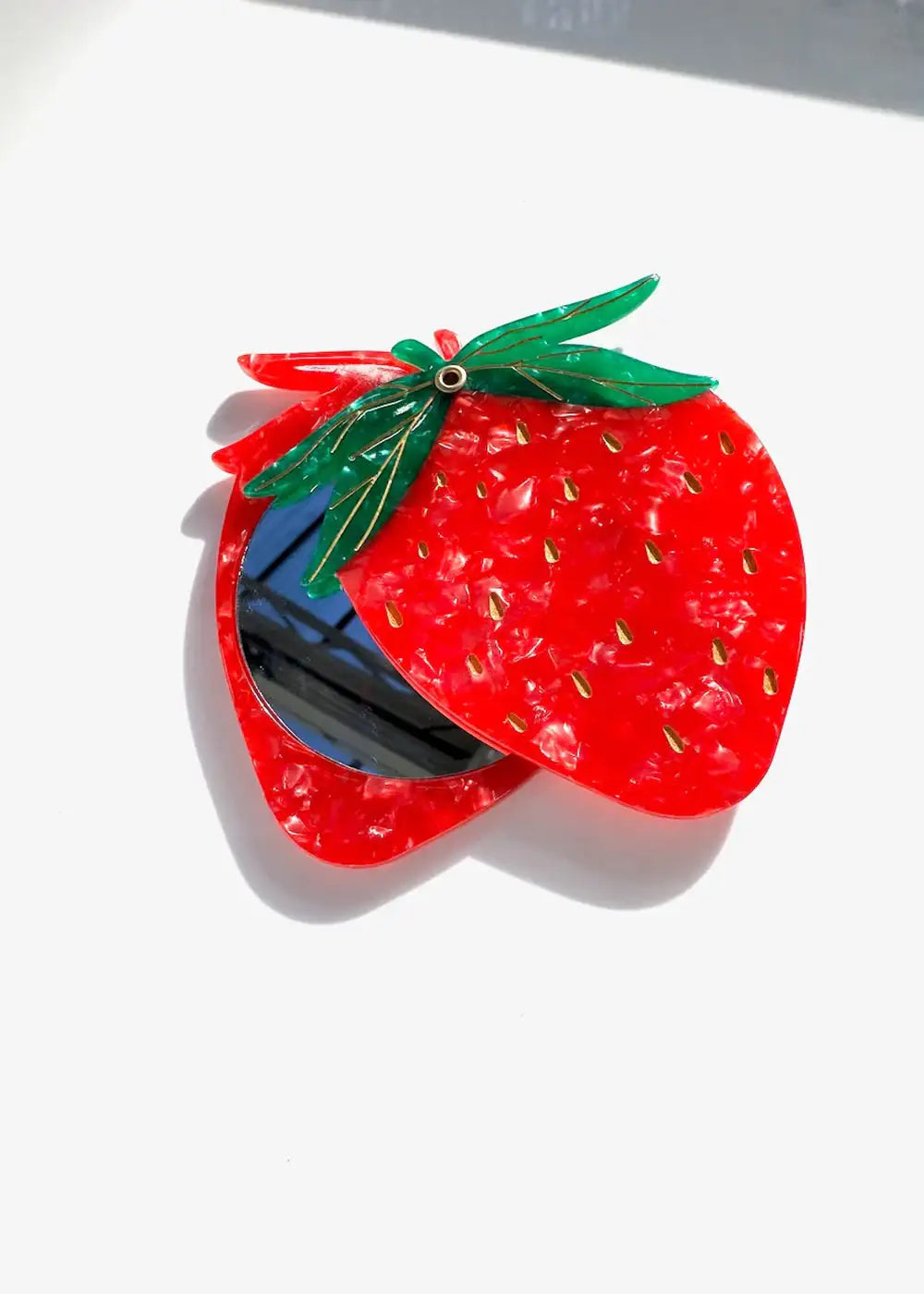 Strawberry-shaped compact mirror with red marbled acrylic and green leaf detail on white background