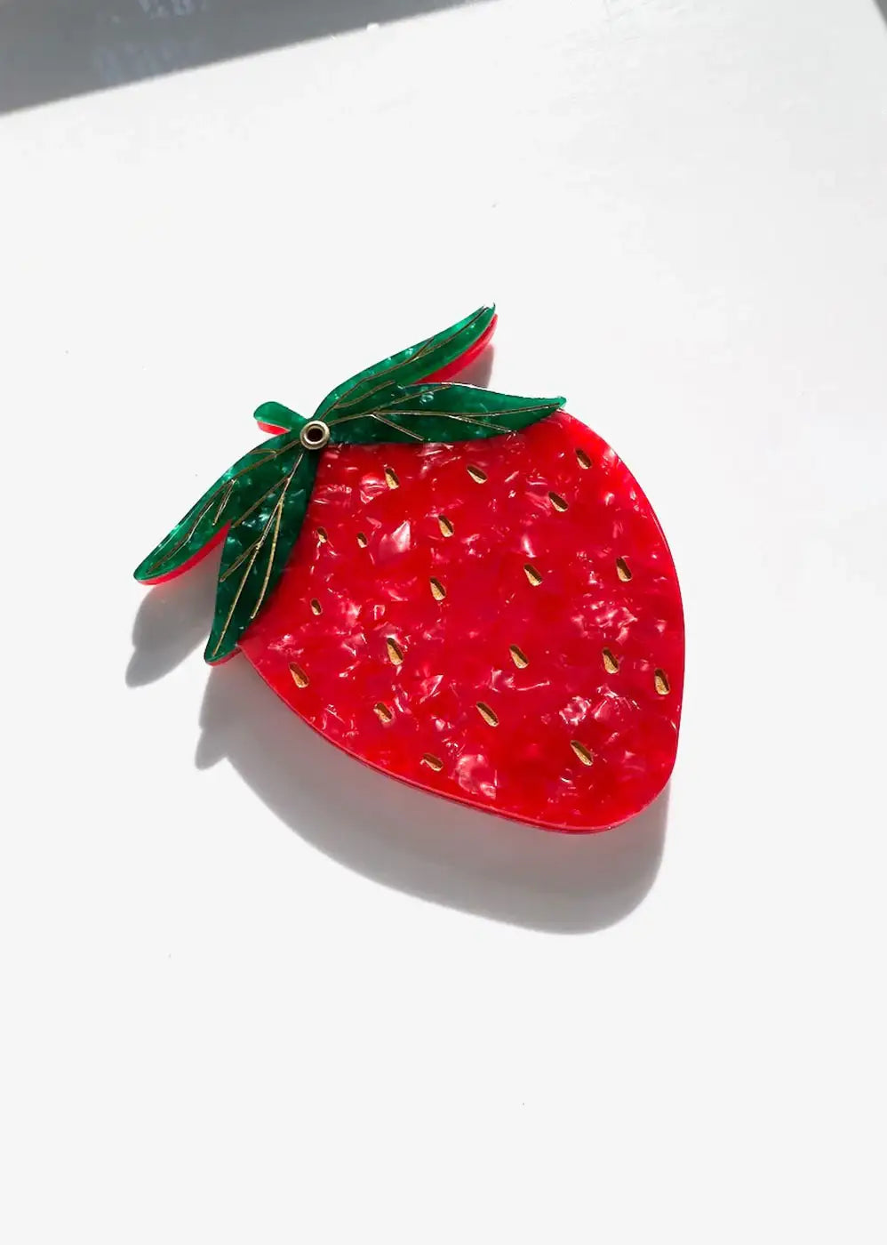 Colorful strawberry-shaped brooch with green leaves and gold seeds on white background