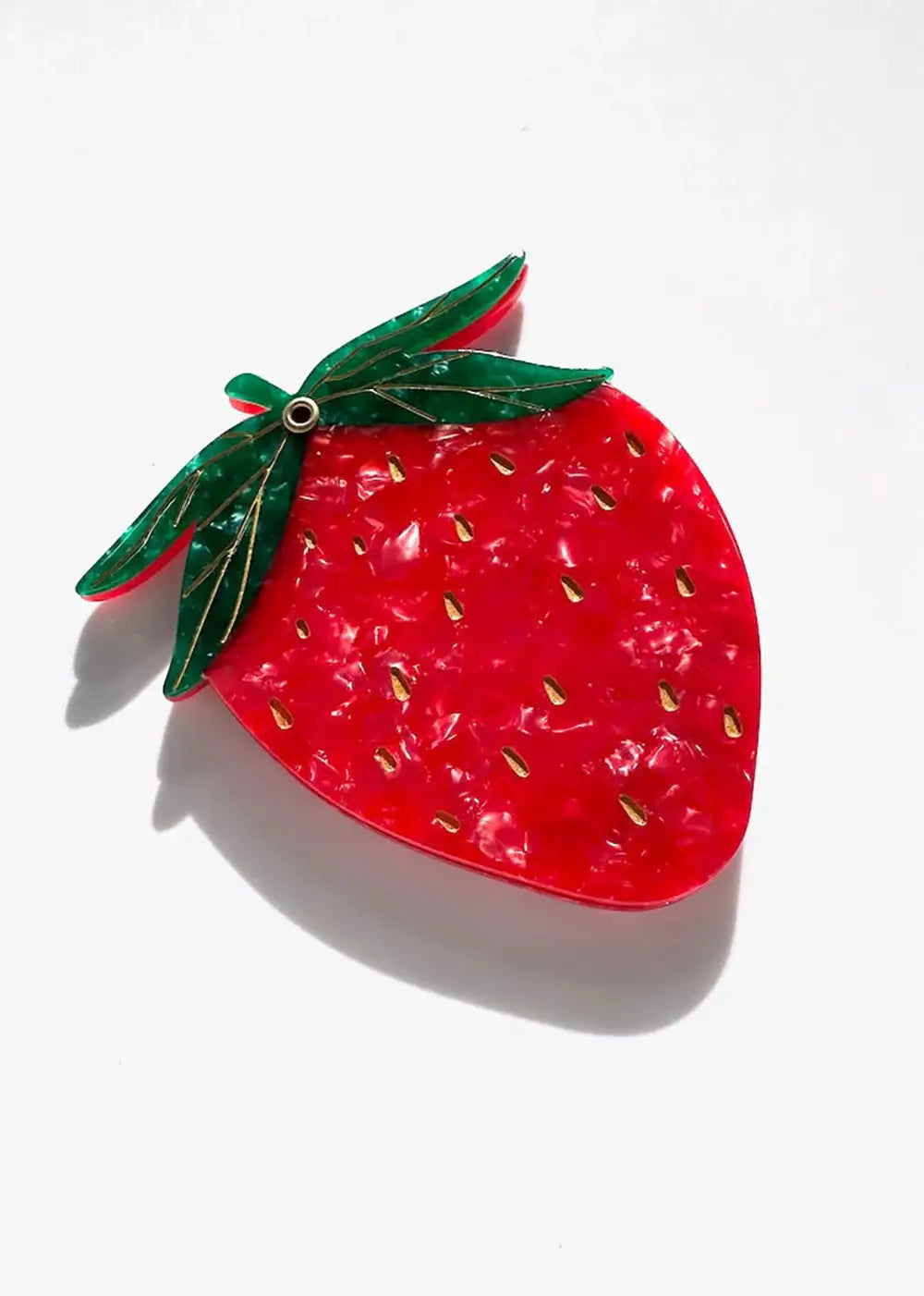 Red strawberry-shaped brooch with green leaf details and gold accents on white background