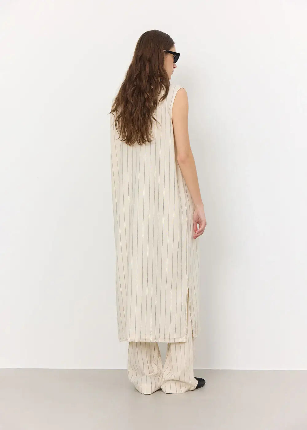 Woman in cream sleeveless pinstripe long tunic and matching wide-leg pants, rear view