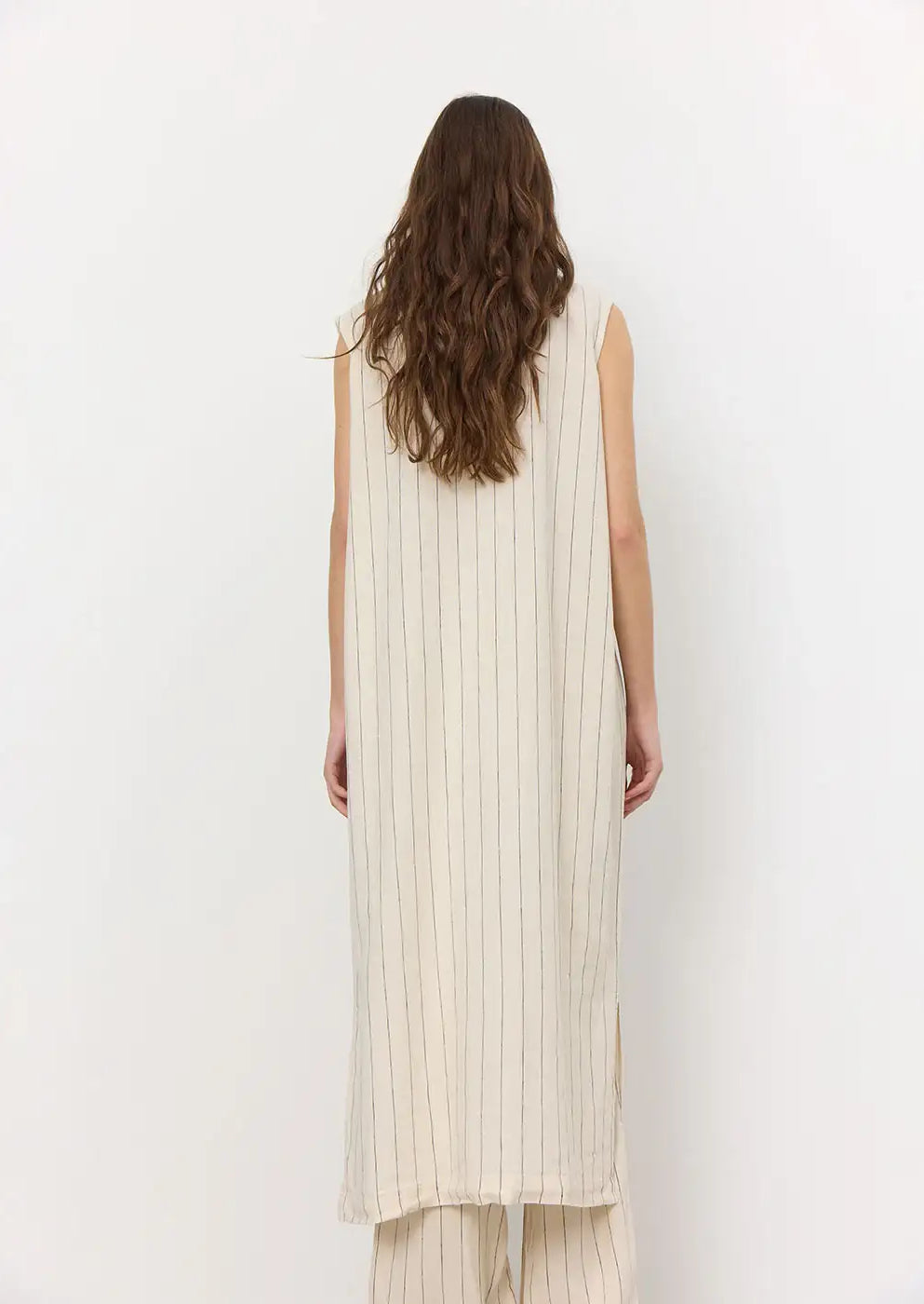Back view of a woman wearing a cream sleeveless long striped dress and matching trousers