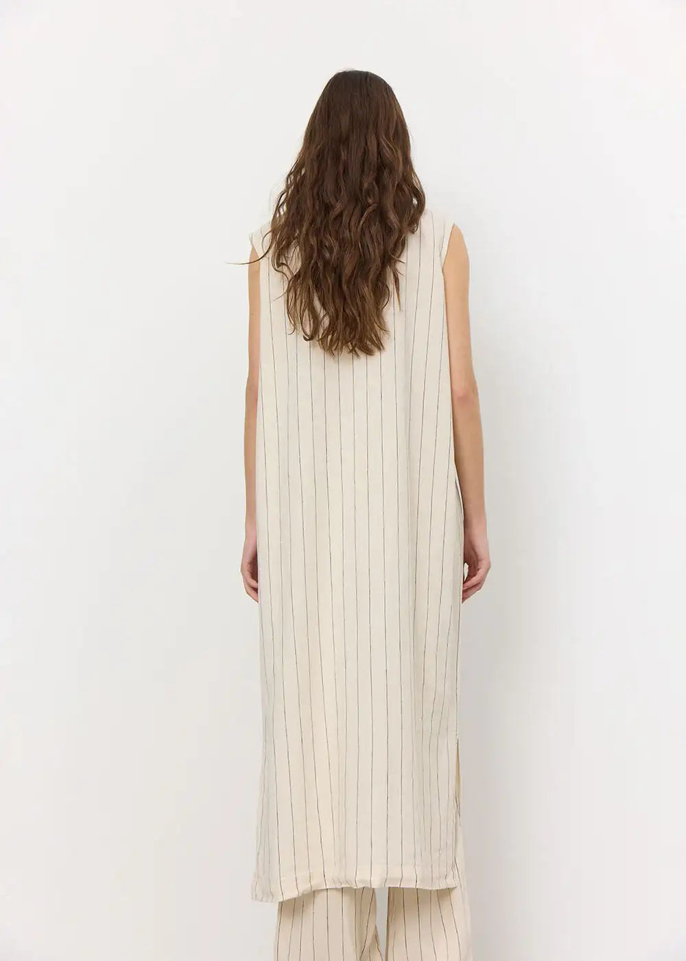 Back view of a woman wearing a cream sleeveless long striped dress and matching trousers