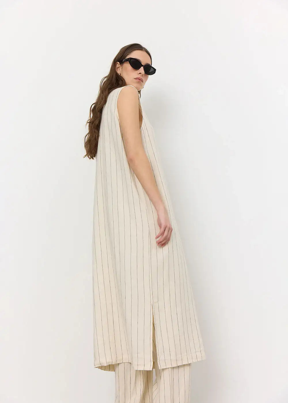 Woman wearing a sleeveless cream pinstripe maxi dress with wide-leg pants and sunglasses
