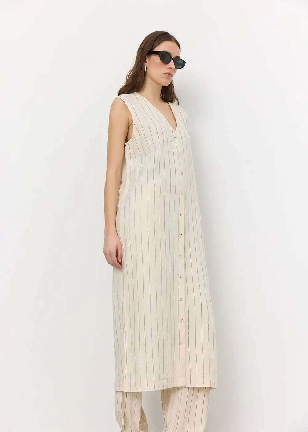 Woman in sleeveless beige striped button-down dress and trousers, minimalist fashion style