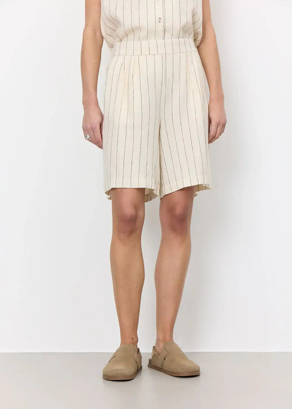 Woman wearing cream pinstripe shorts, casual top, and beige slip-on shoes