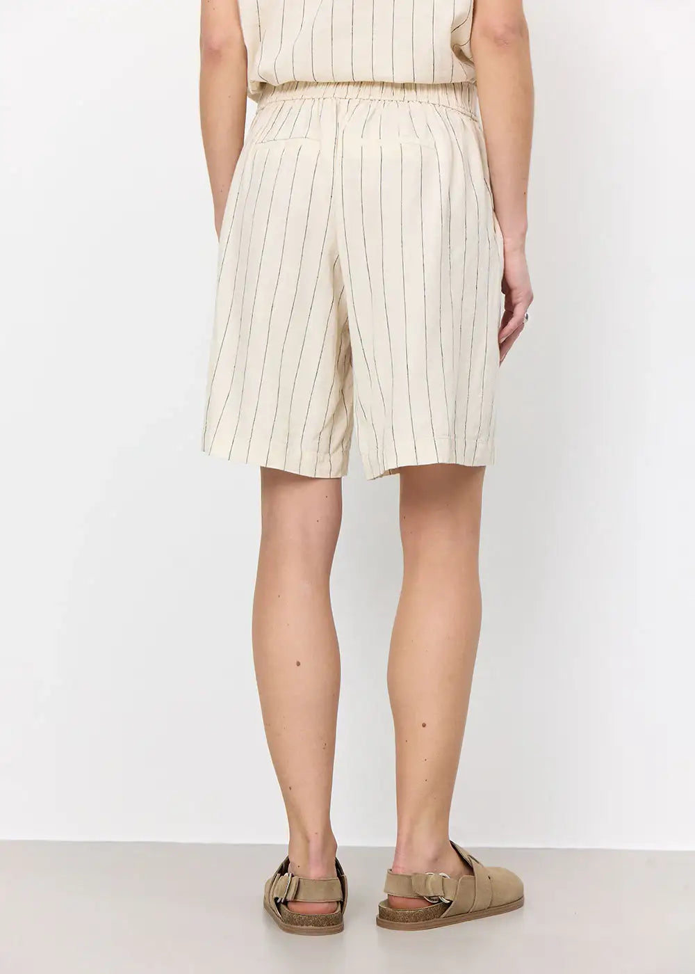 Back view of beige pinstripe shorts with elastic waist, paired with tan sandals