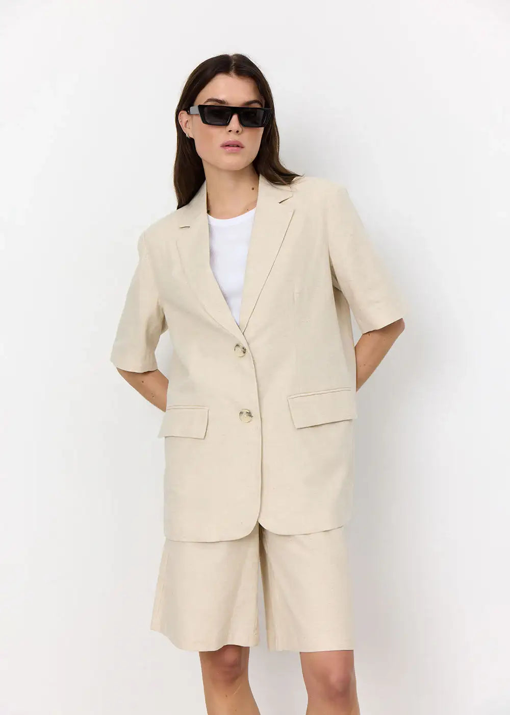 Woman in beige short sleeve blazer and matching shorts with sunglasses, studio fashion shot