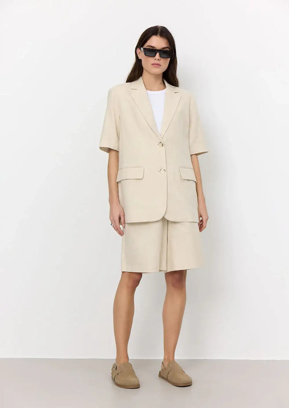 Woman in beige oversized blazer and matching tailored shorts, white t-shirt, loafers, sunglasses