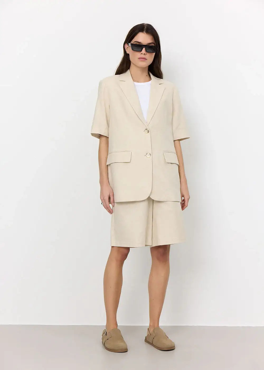 Woman in beige oversized blazer and matching tailored shorts, white t-shirt, loafers, sunglasses