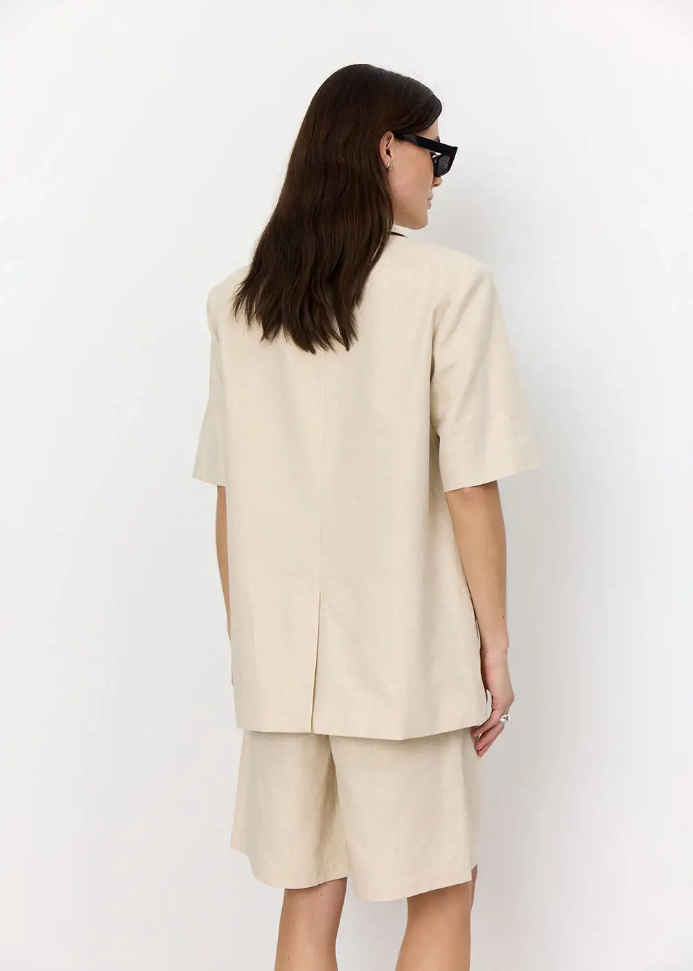 Woman wearing beige oversized shorts suit with short sleeves, viewed from the back