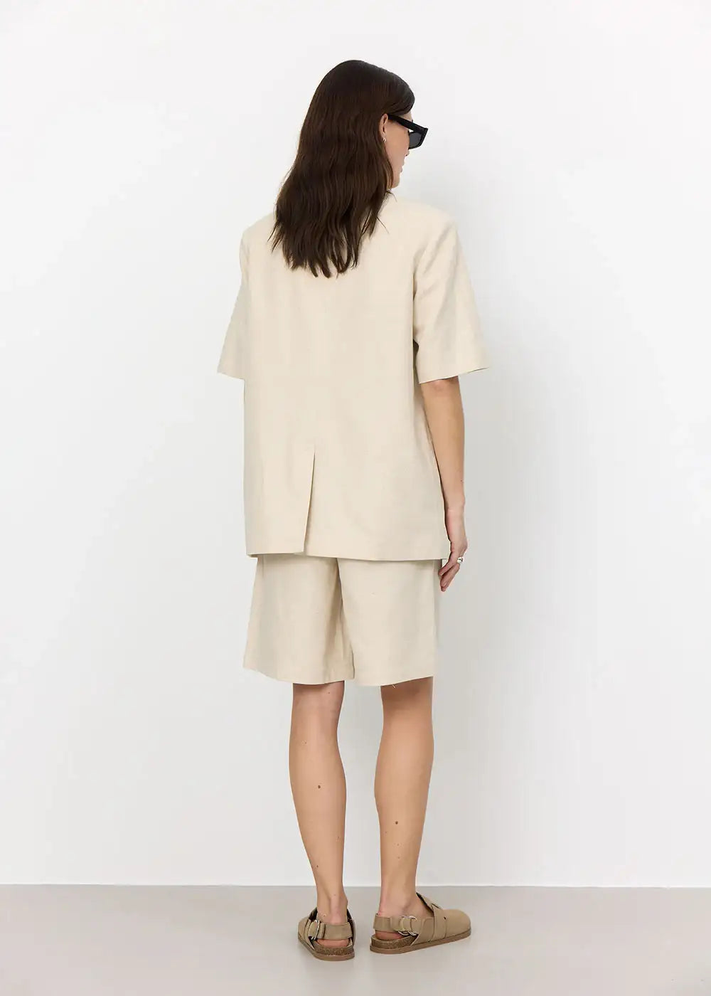 Woman wearing beige oversized blazer and matching shorts, standing in minimalist room