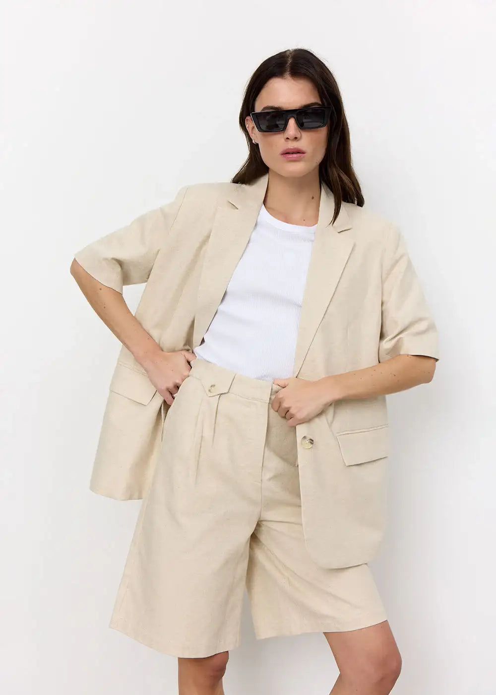 Woman wearing beige short-sleeve blazer and tailored shorts with white top and sunglasses
