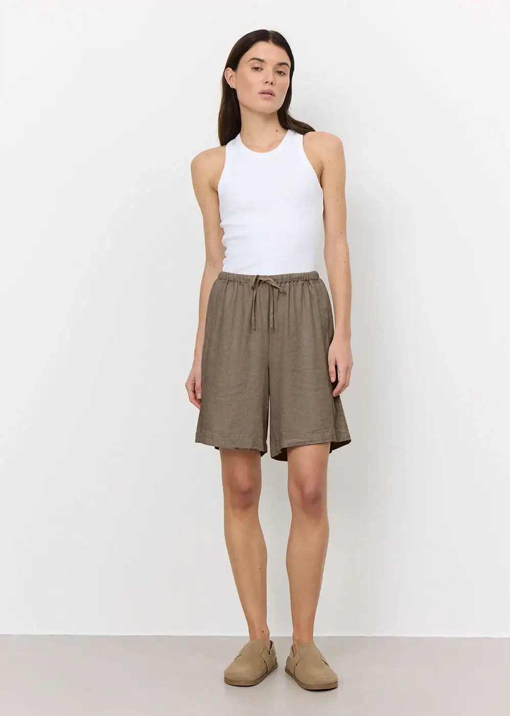 Woman wearing a white sleeveless tank top and loose brown linen shorts with drawstring waist