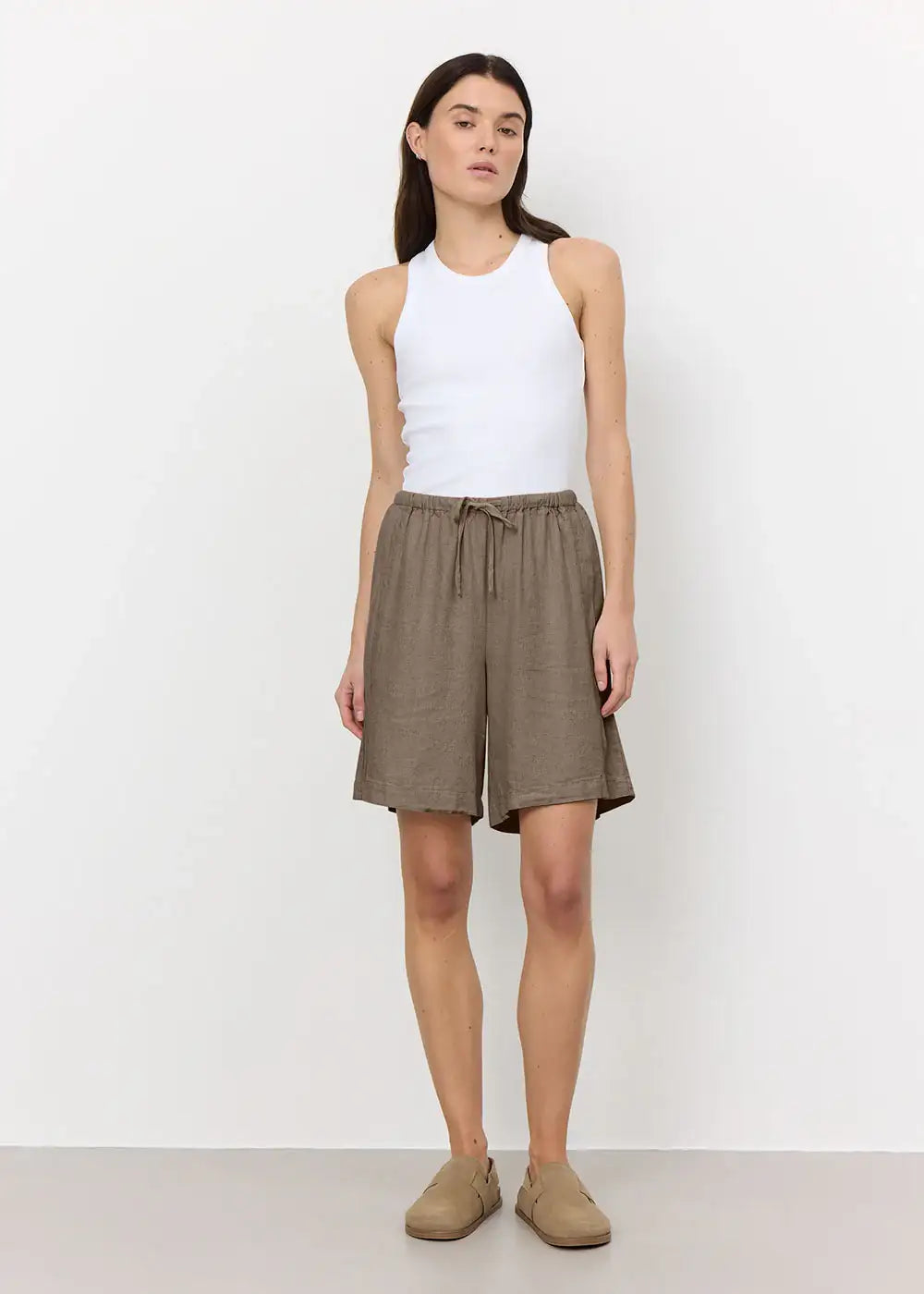 Woman wearing a white sleeveless tank top and loose brown linen shorts with drawstring waist