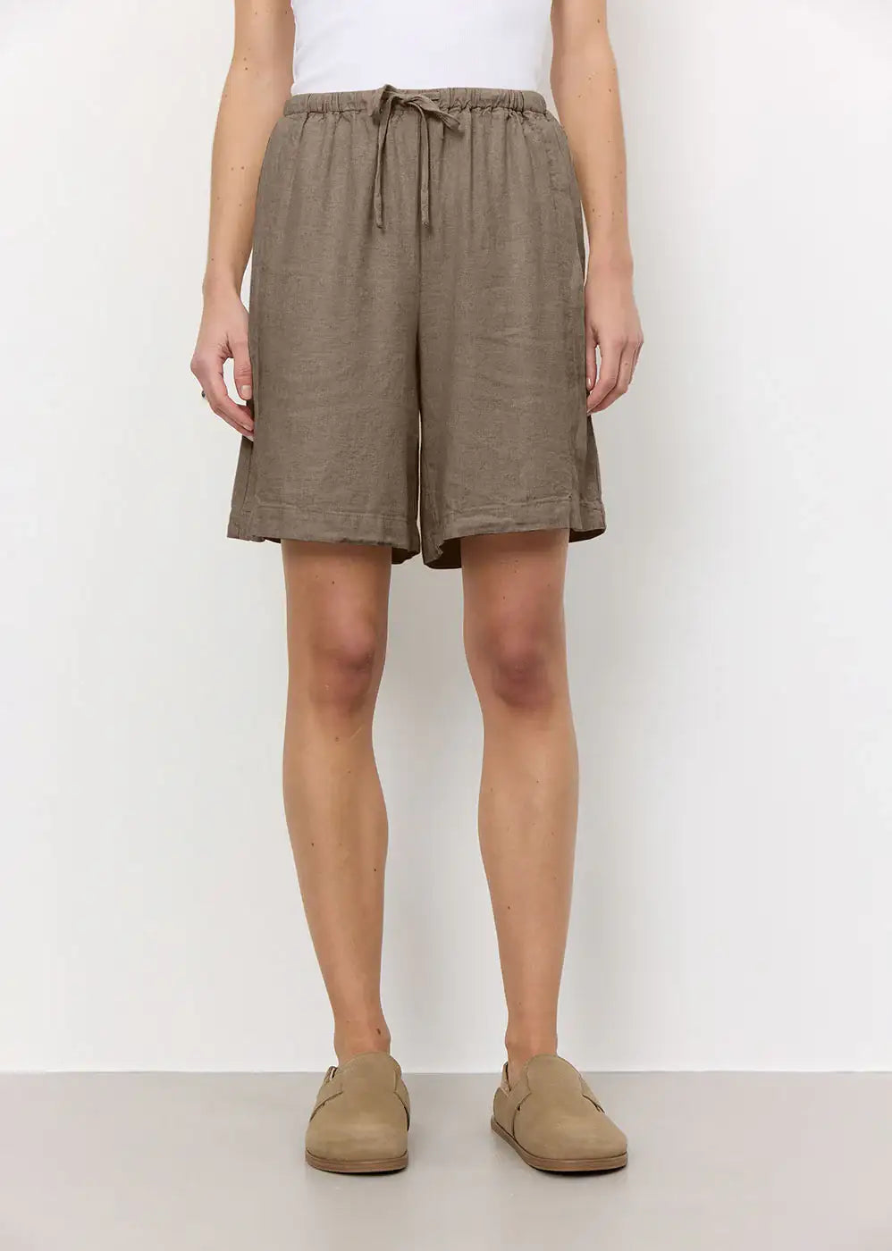 Woman wearing loose brown linen shorts with drawstring waist and casual beige shoes