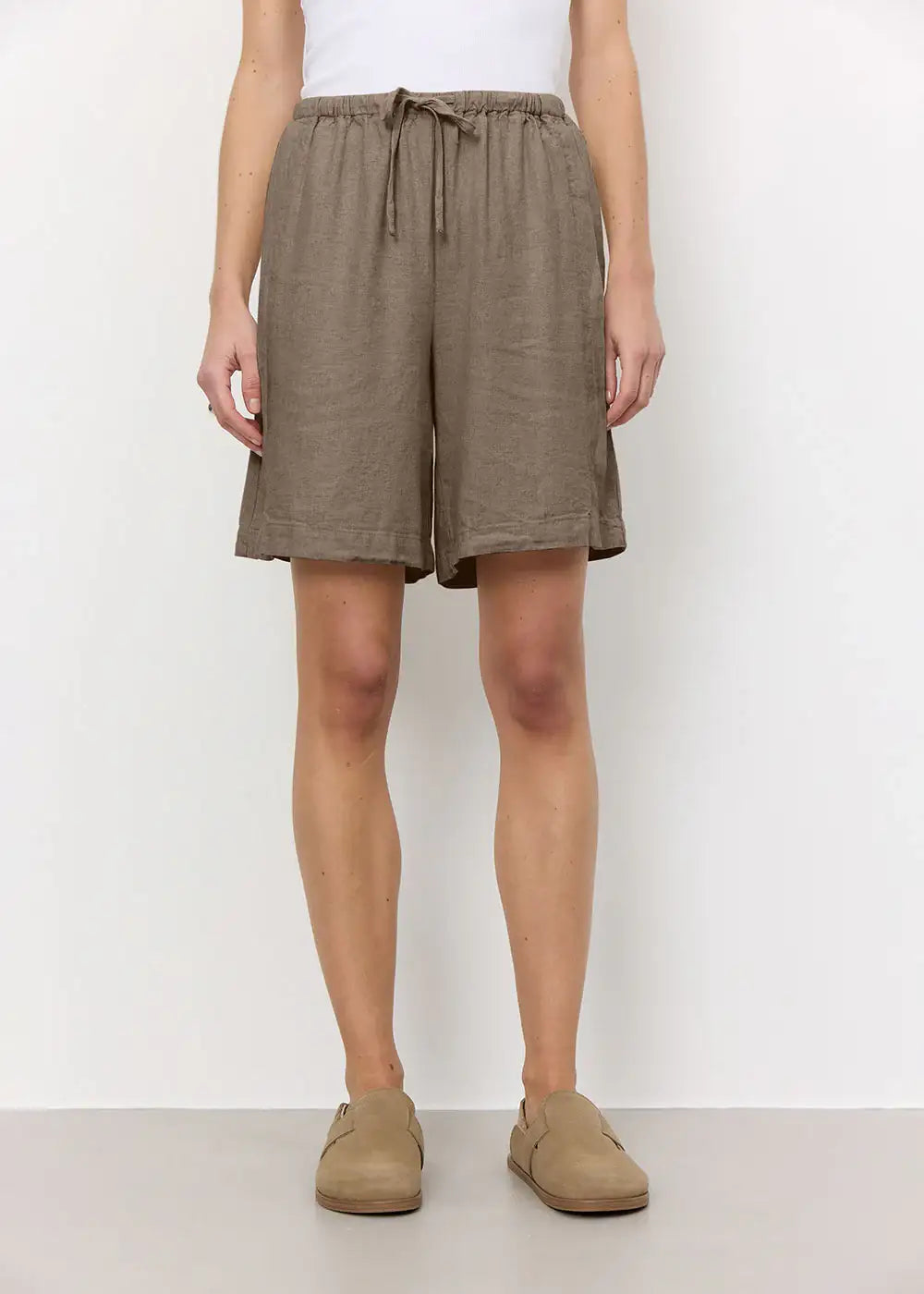 Woman wearing loose brown linen shorts with drawstring waist and casual beige shoes