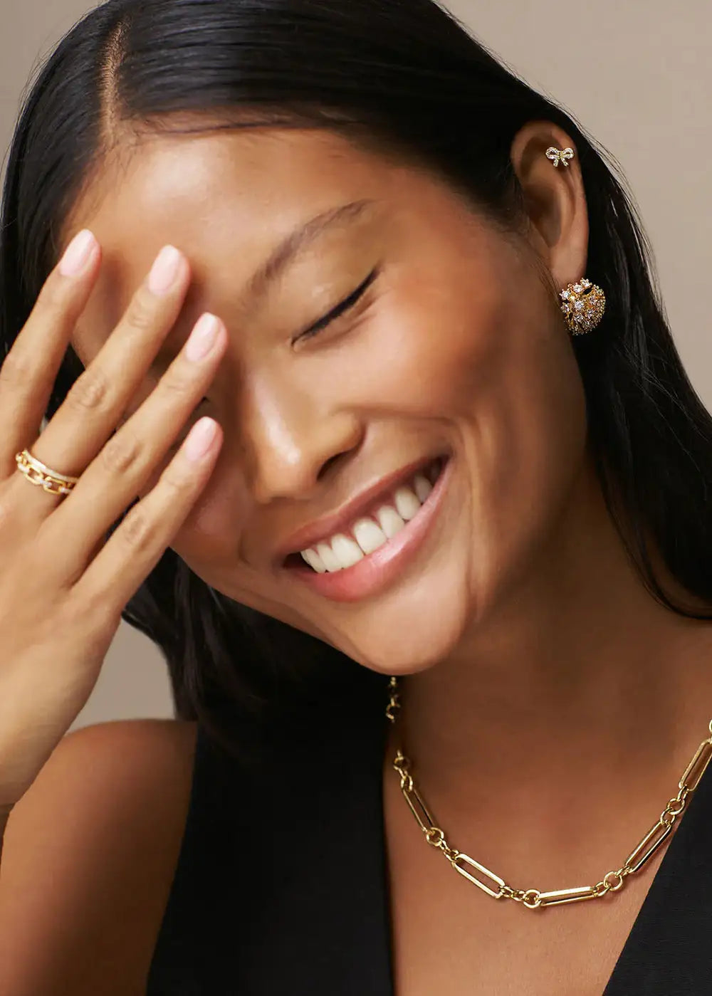Smiling woman wearing gold chain necklace, gold earrings, and gold ring.