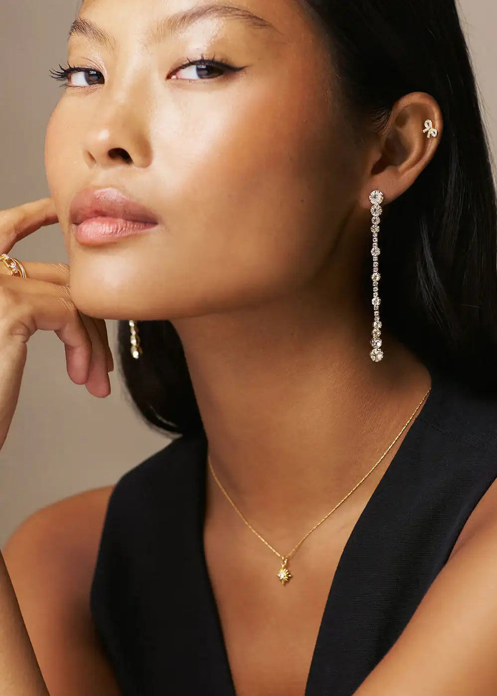 Woman wearing long crystal drop earrings, gold pendant necklace and black top