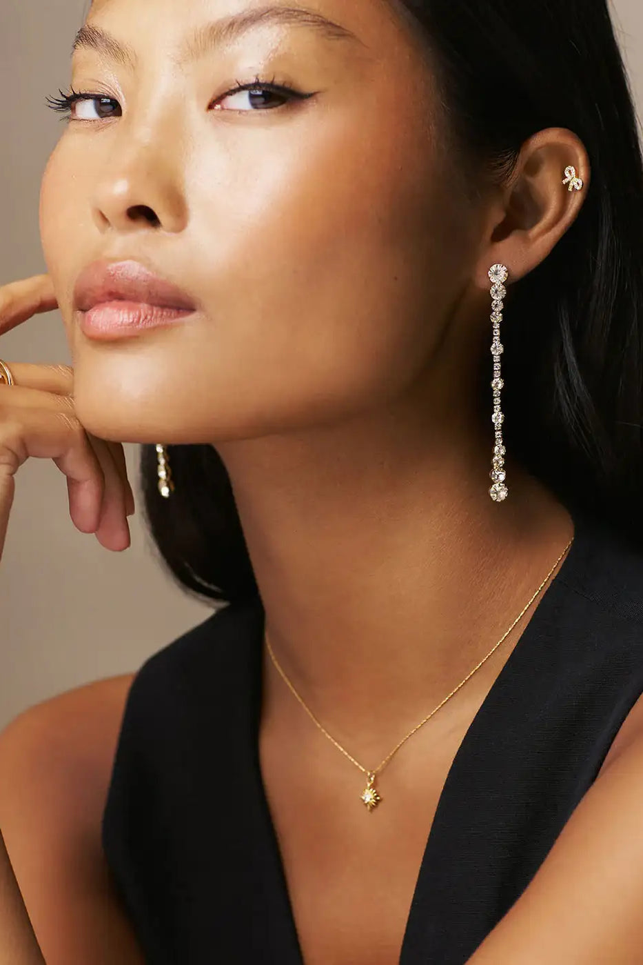 Woman wearing long crystal drop earrings, gold pendant necklace and black top