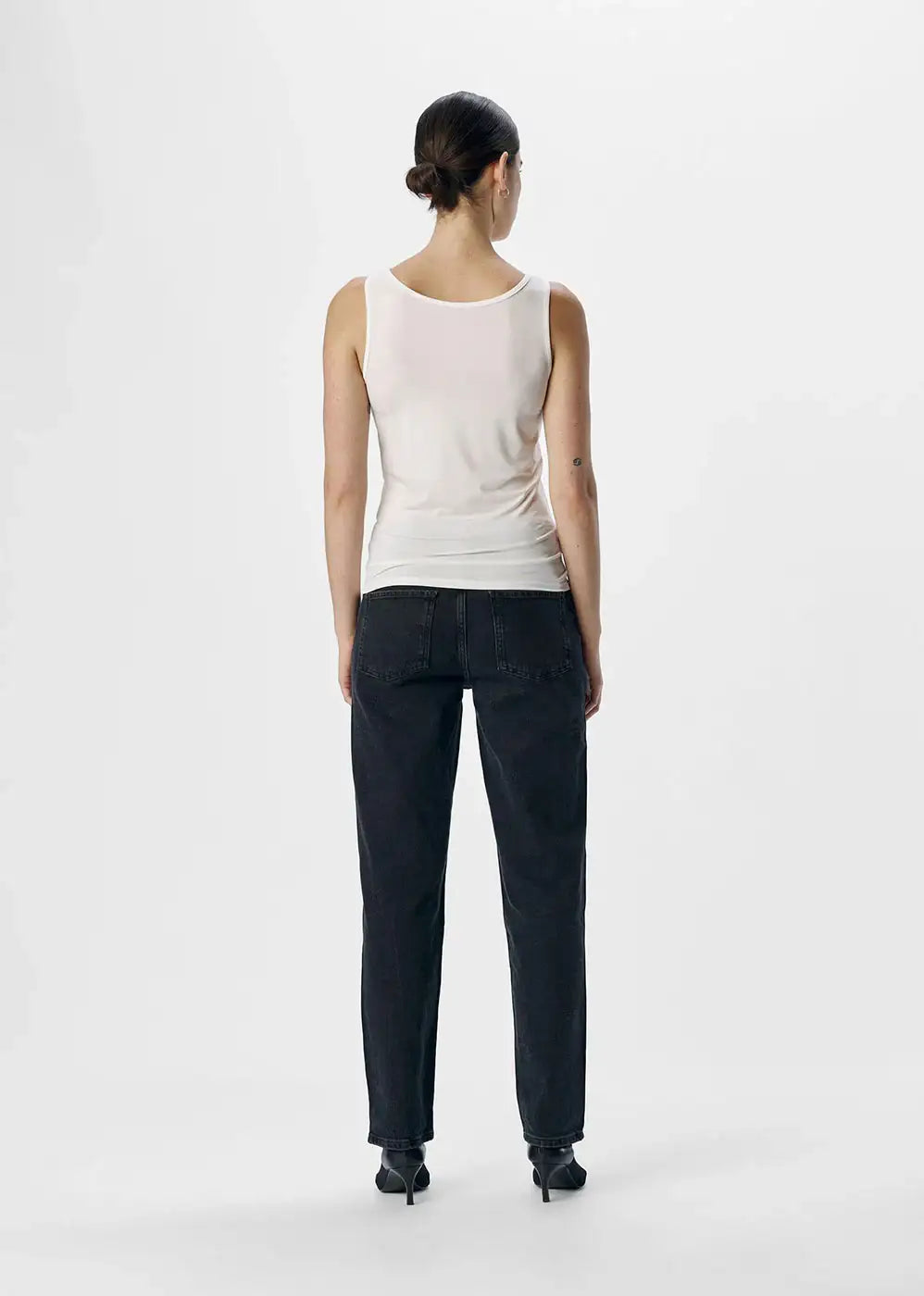 Woman in white sleeveless tank top and black jeans, back view, minimalist studio