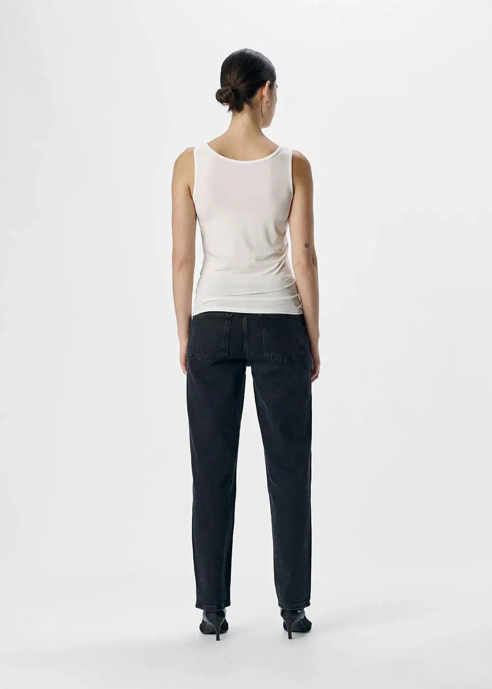 Woman in white sleeveless tank top and black jeans, back view, minimalist studio