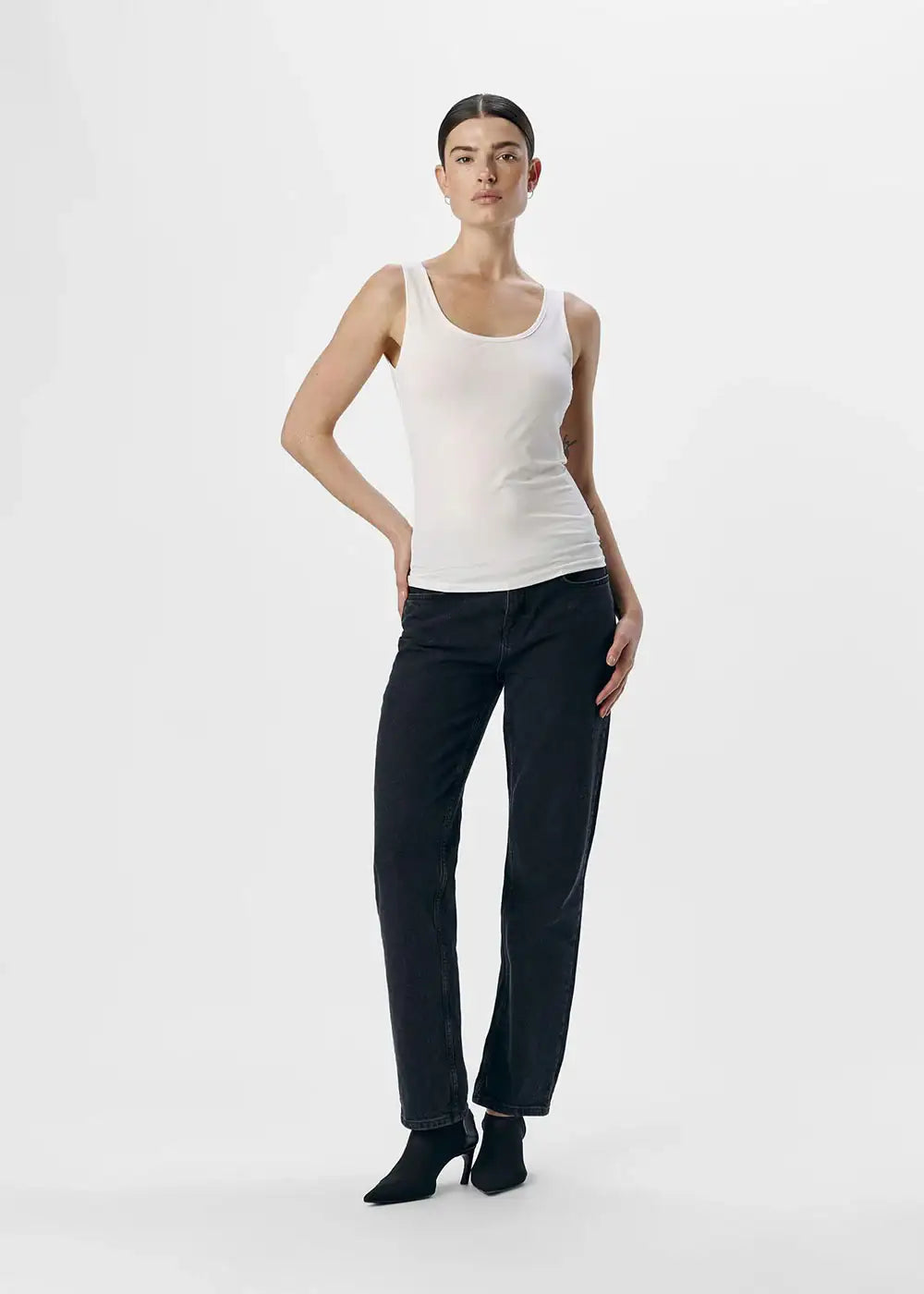 Woman wearing a white fitted tank top and black jeans, fashion studio shot