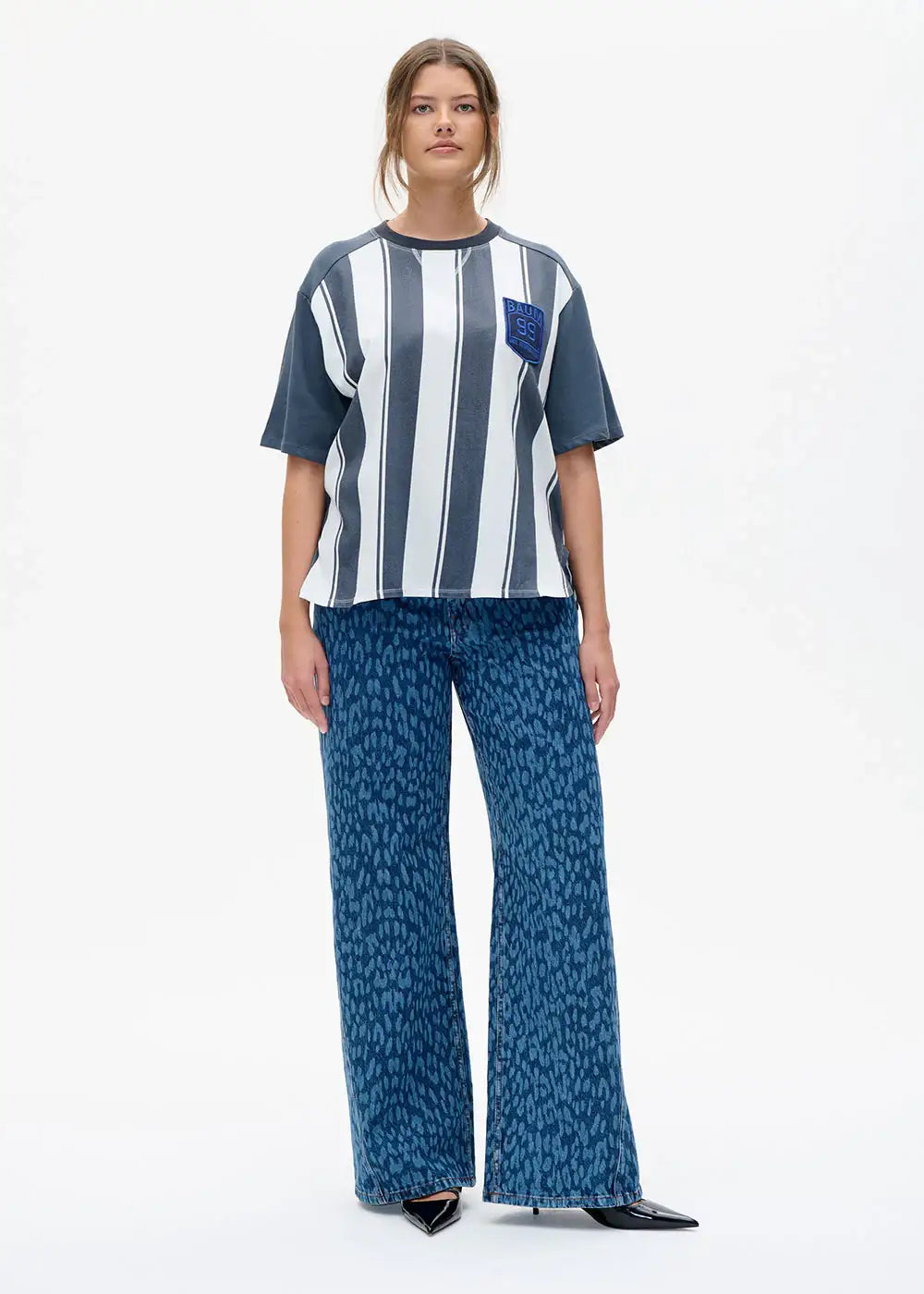 Woman wearing a striped oversized t-shirt with badge and wide-leg blue animal print jeans