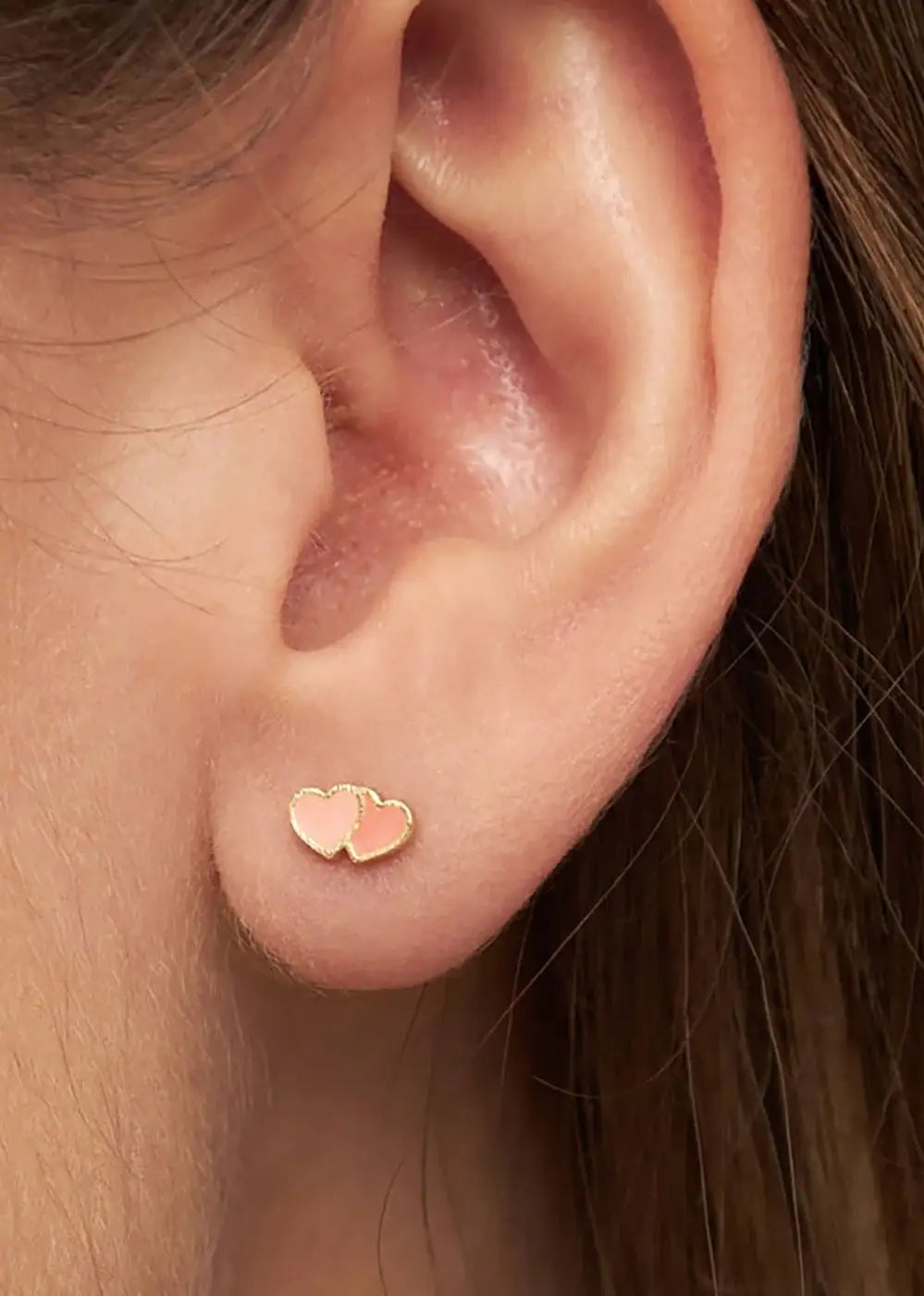 Gold plated stud earring with two coral pink hearts on ear lobe