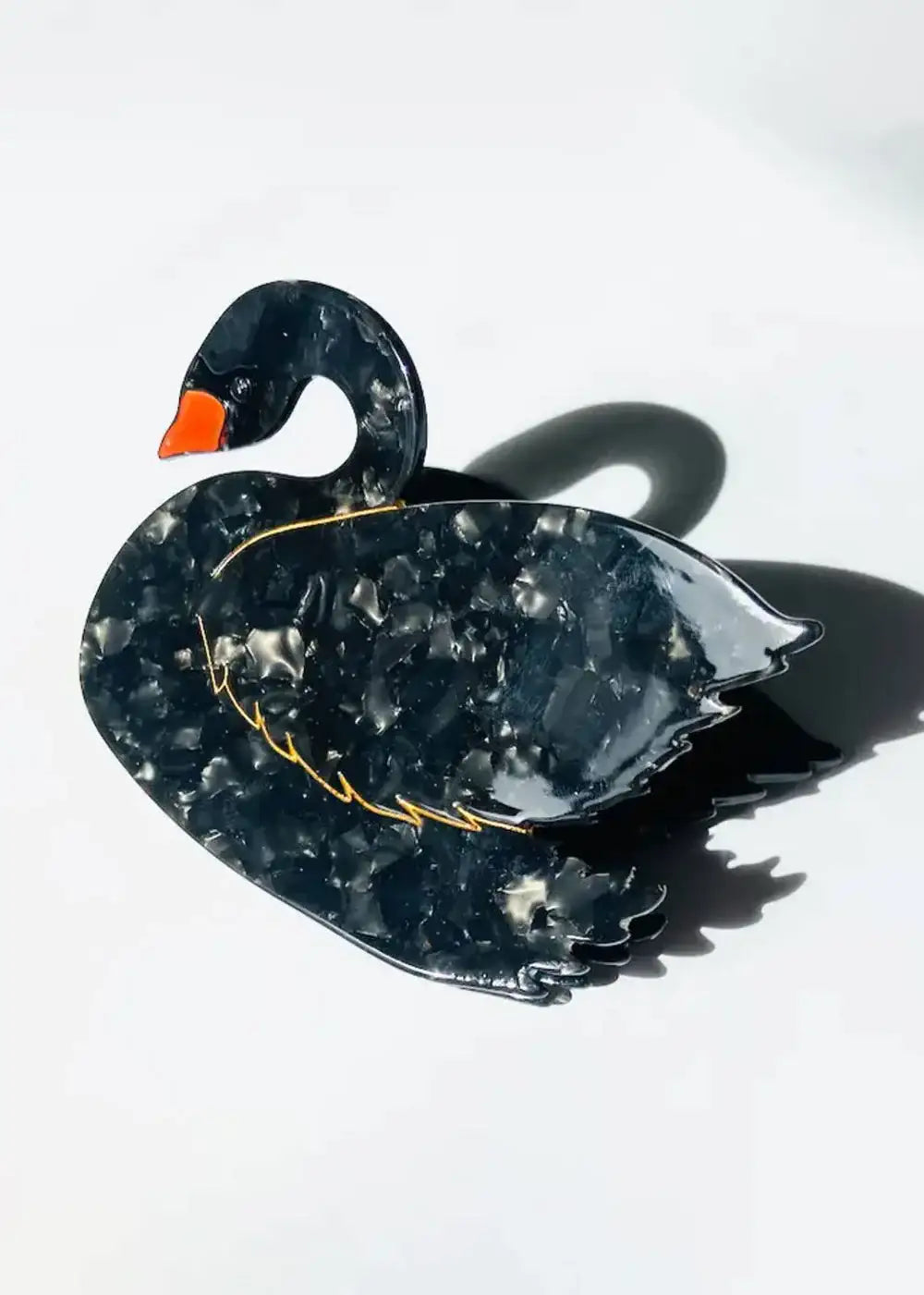 Black swan brooch with marbled texture and orange beak on white background