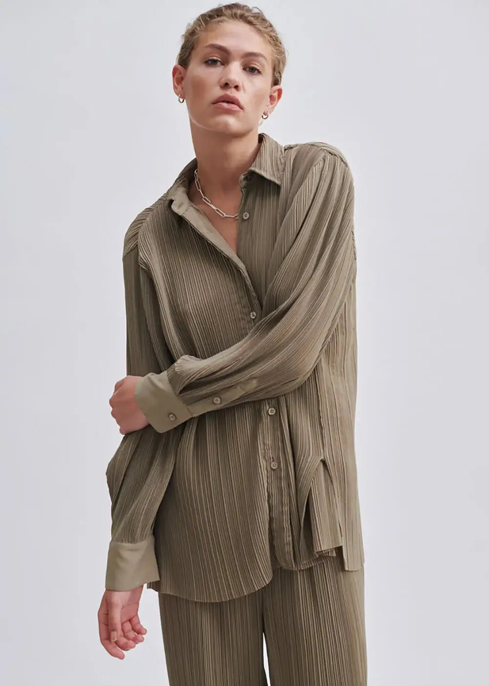 Woman wearing olive green pleated shirt and matching trousers in minimalist studio
