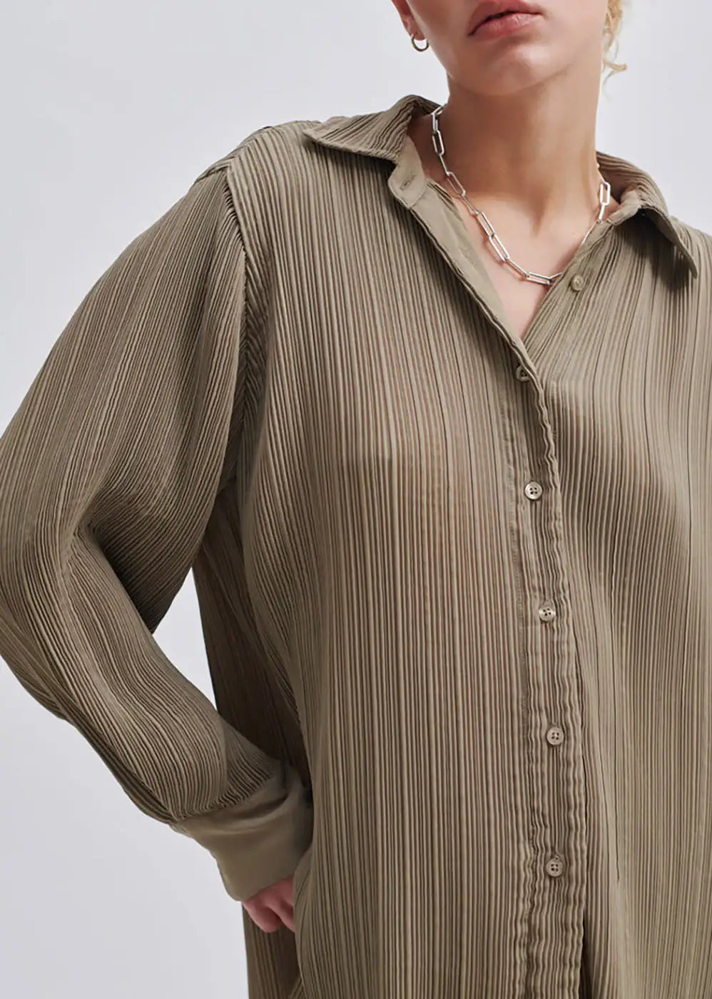 Woman wearing a taupe pleated button-up shirt with a silver chain necklace