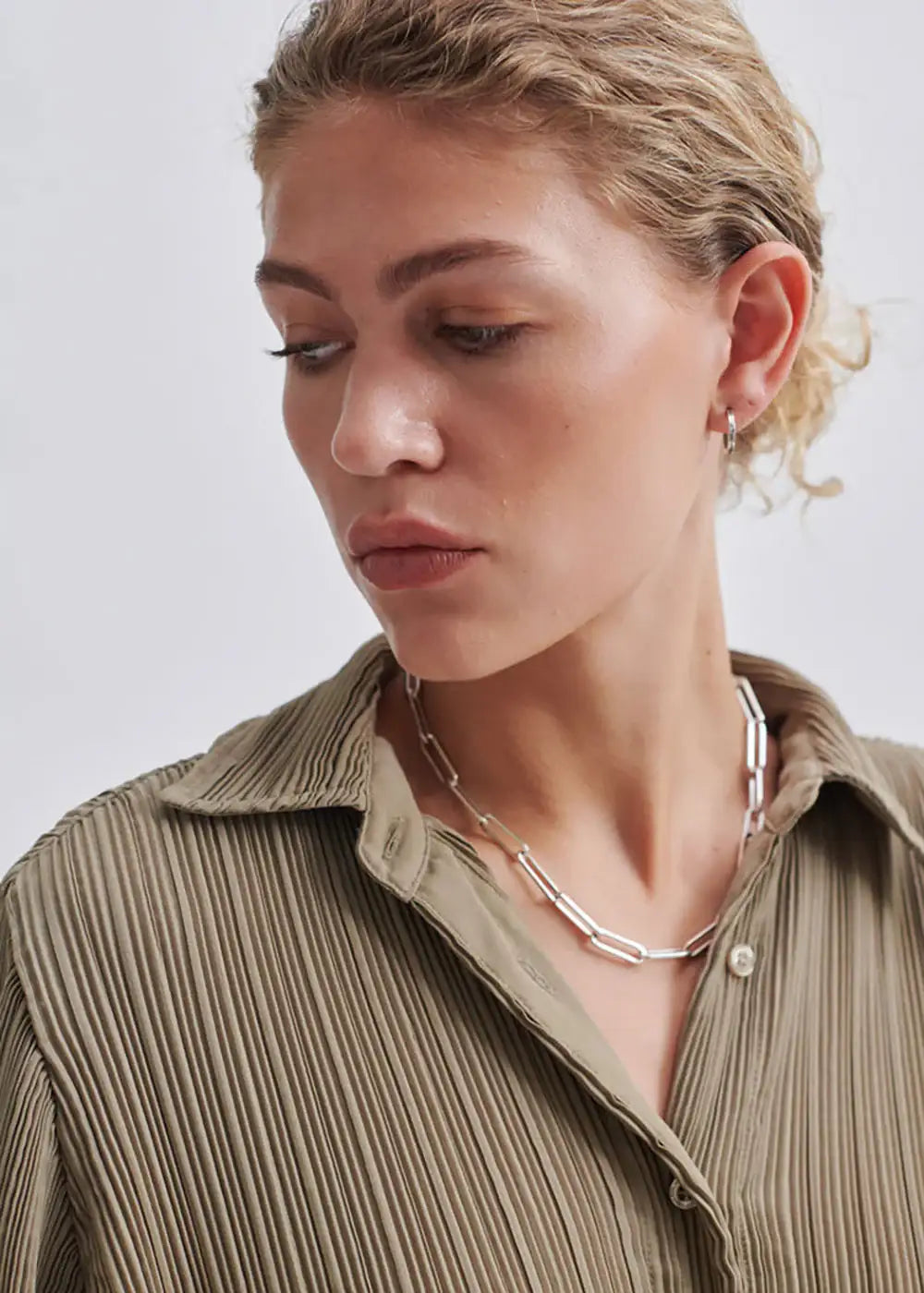 Woman wearing a pleated khaki shirt with chunky silver chain necklace and hoop earring
