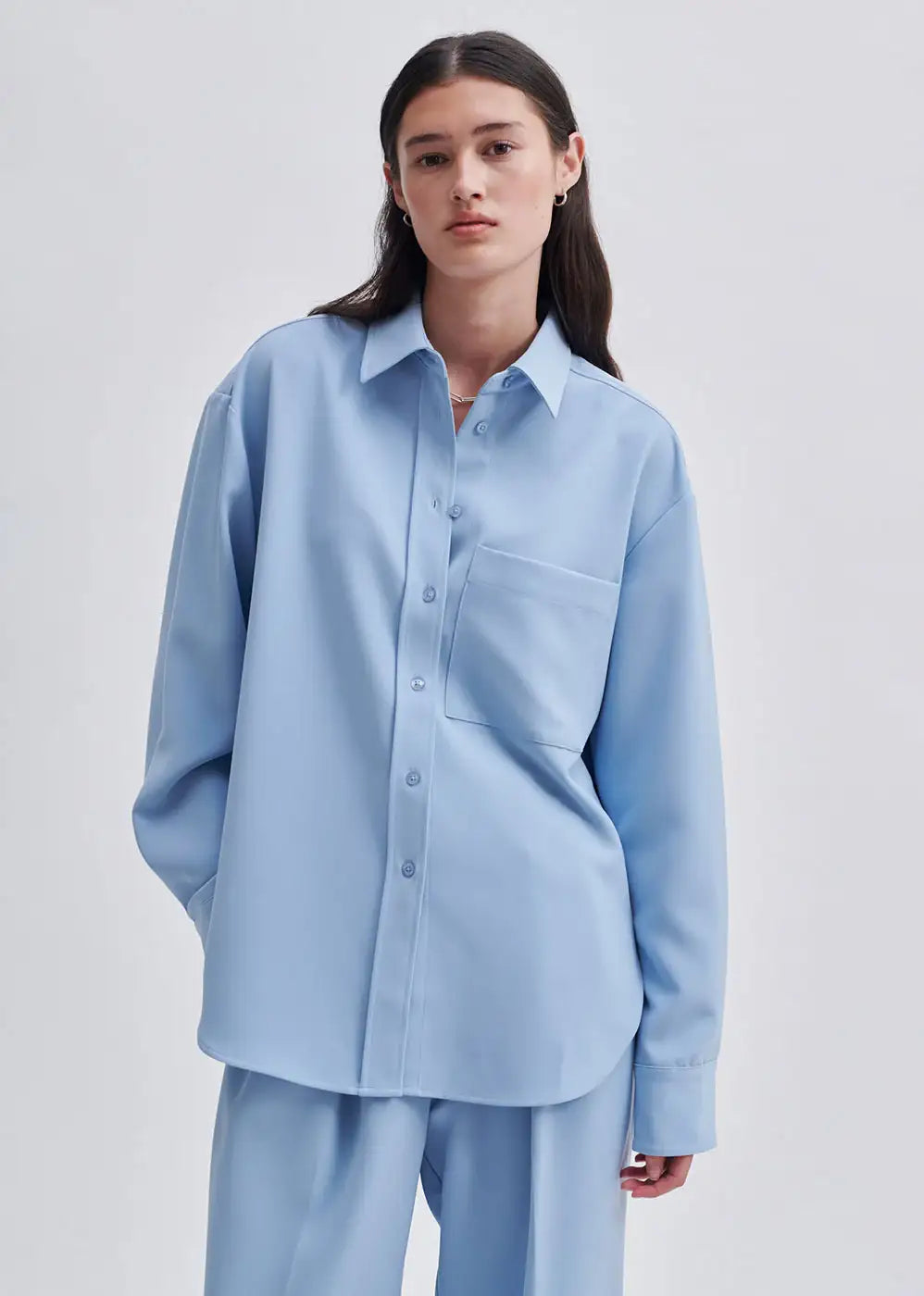 Woman wearing loose fit light blue button-up shirt and matching trousers, minimalist style