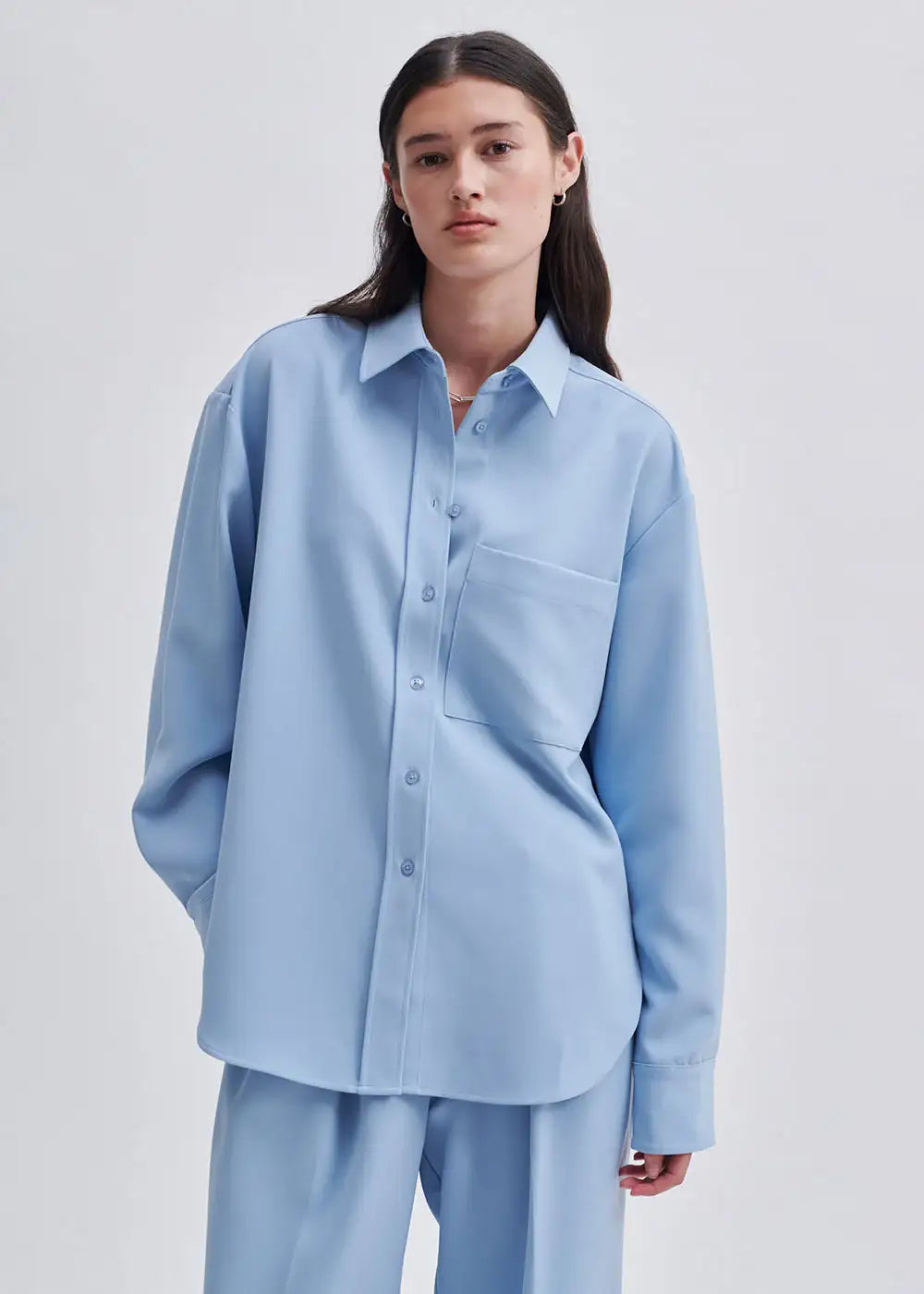 Woman wearing loose fit light blue button-up shirt and matching trousers, minimalist style