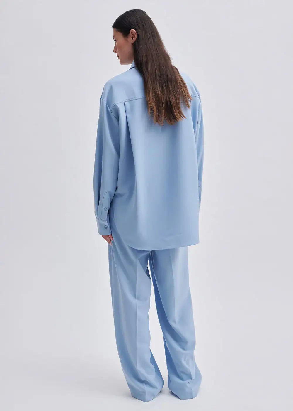 Woman wearing loose light blue shirt and matching wide-leg trousers, back view
