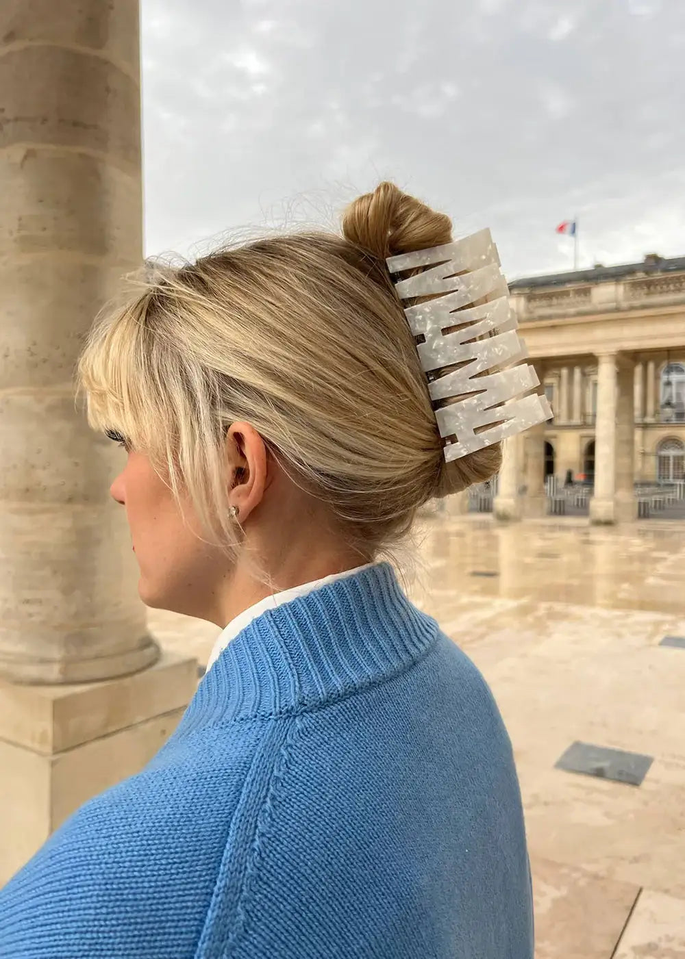 Woman in blue sweater wearing a large marble hair clip with blonde hair in a bun outdoors