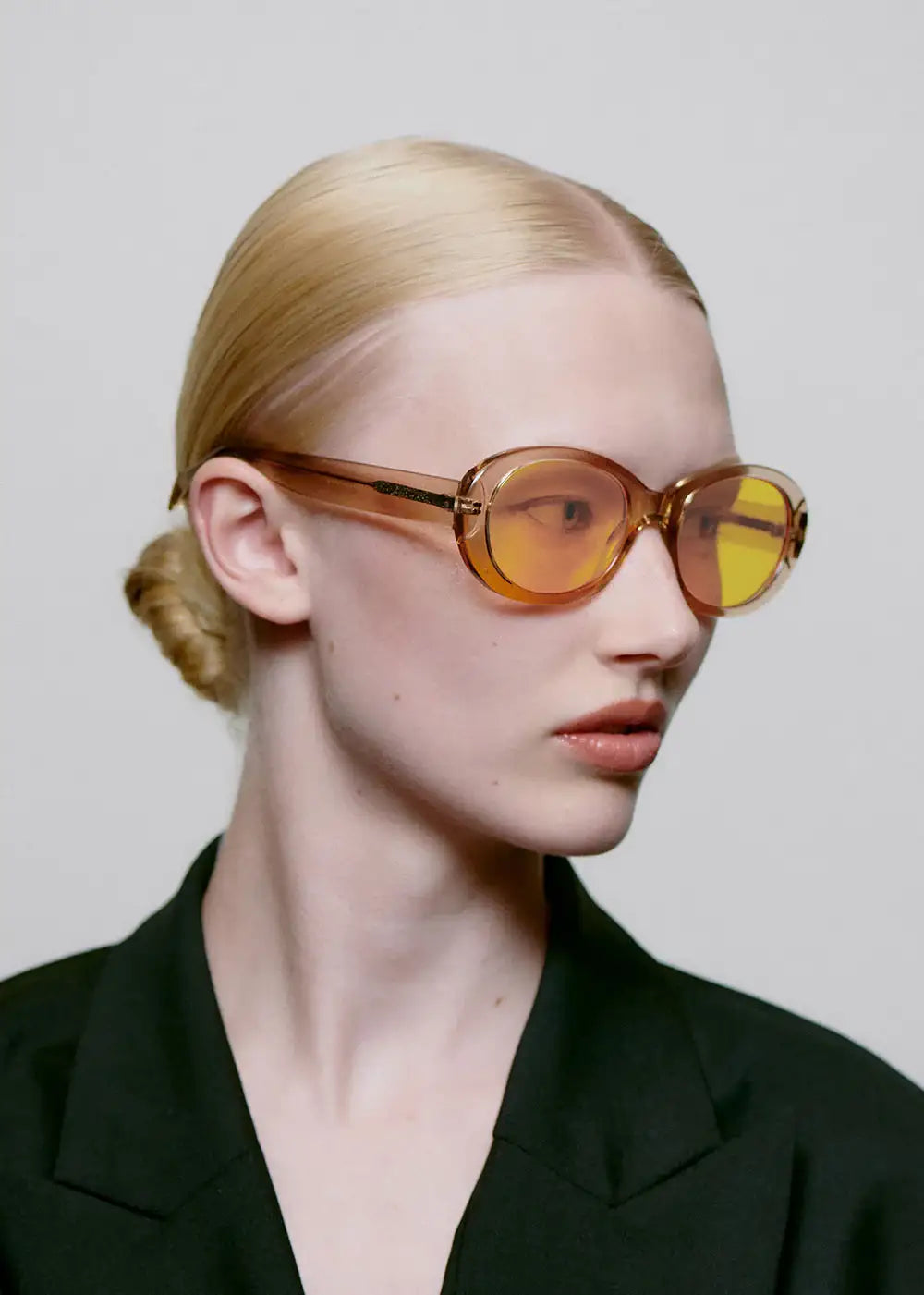 Woman wearing oversized oval champagne sunglasses and black blazer with slicked-back hair