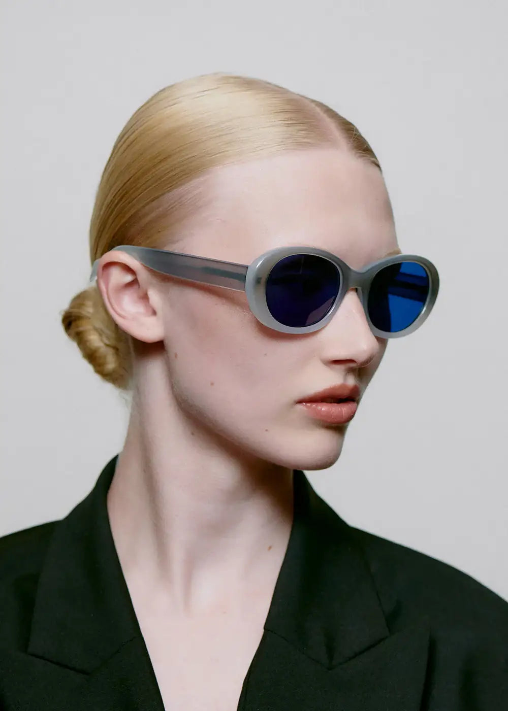 Woman wearing oval grey frame sunglasses with blue lenses and black blazer, side profile