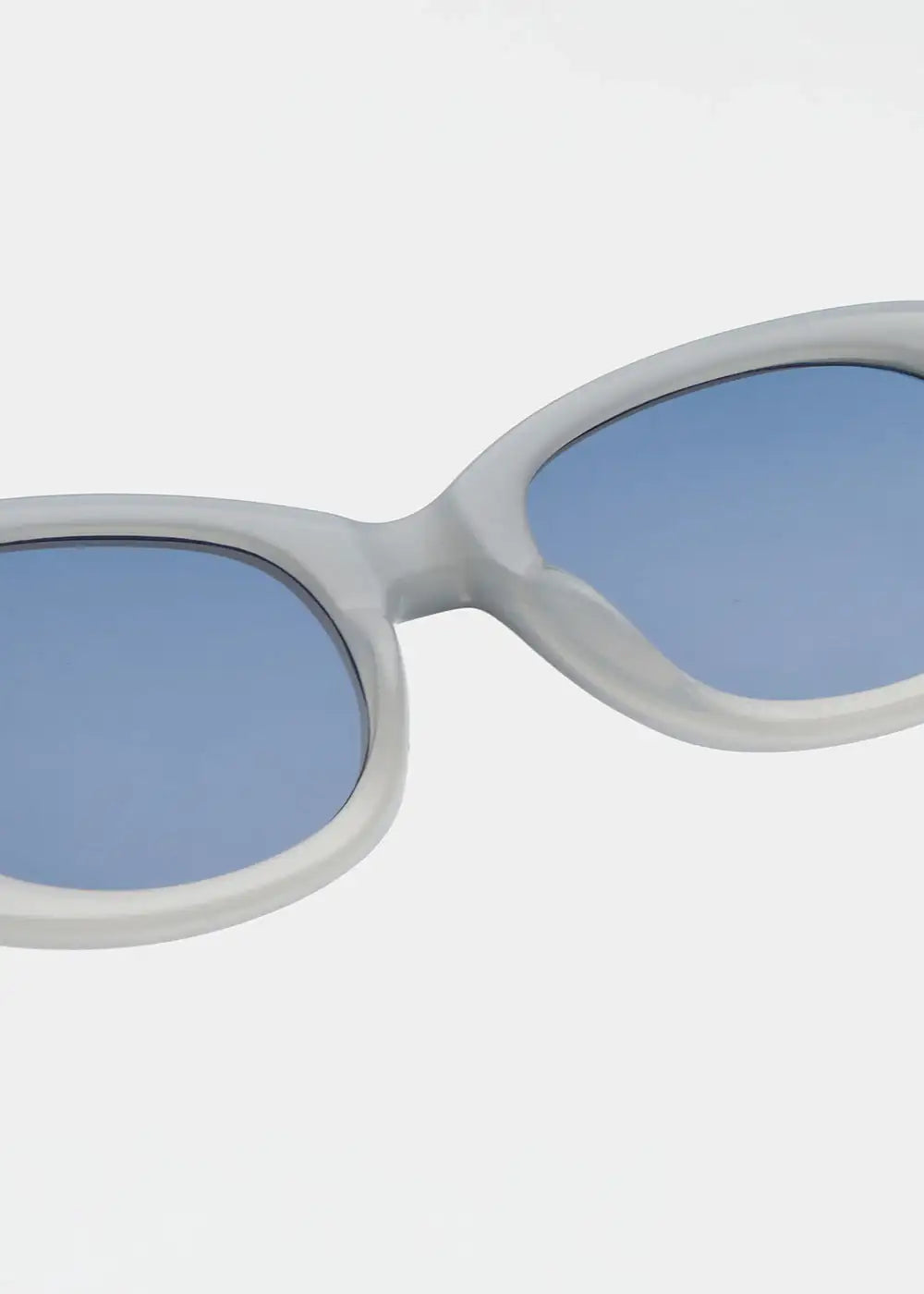 Close-up of light grey sunglasses with blue tinted oval lenses on white background