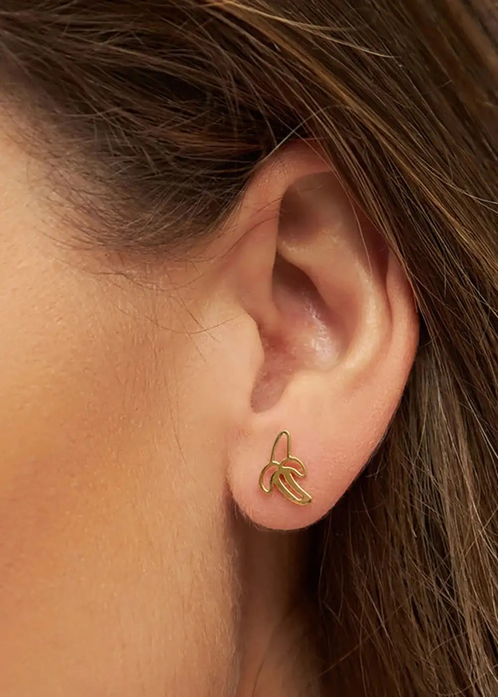 Gold plated banana-shaped ear stud earring worn on a woman's ear