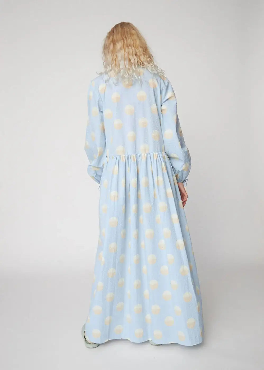 Woman wearing a light blue maxi dress with large white polka dots, back view