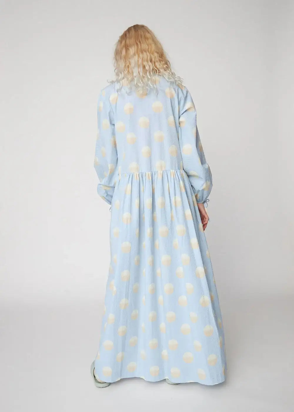 Woman wearing a light blue maxi dress with large white polka dots, back view