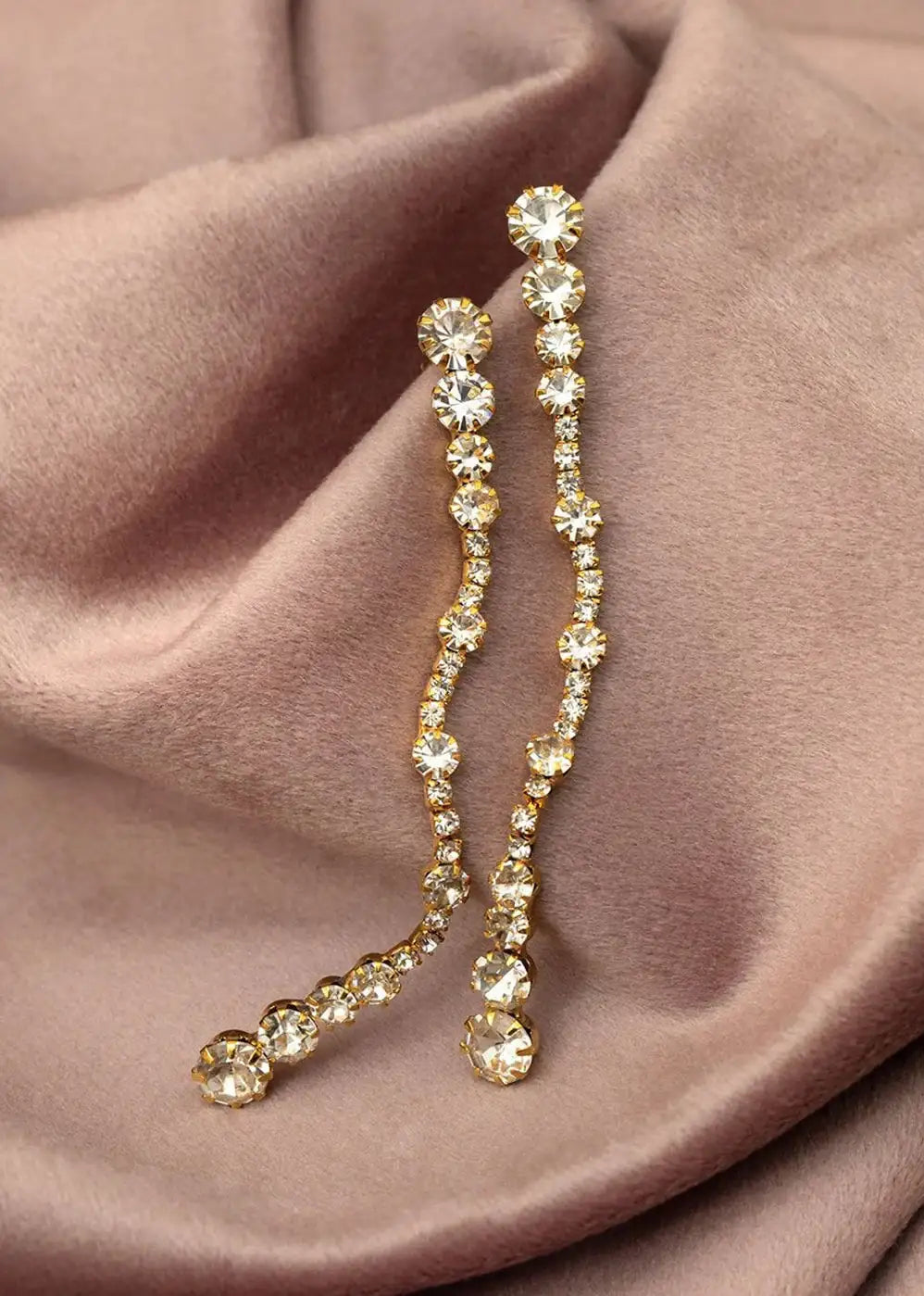 Gold crystal drop earrings with round clear stones on taupe fabric background