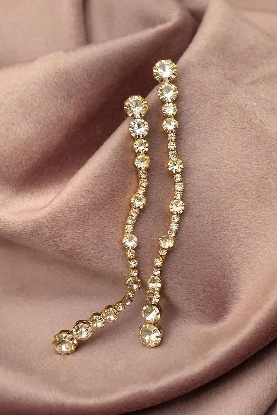 Gold crystal drop earrings with round clear stones on taupe fabric background