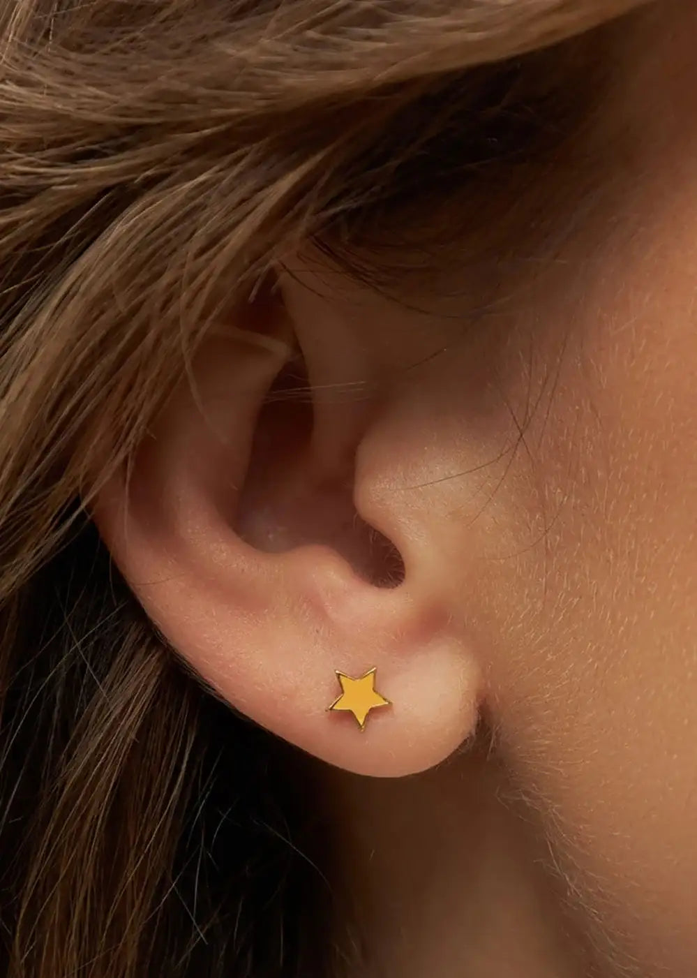 Gold plated star-shaped stud earring worn on ear, minimalist jewelry style