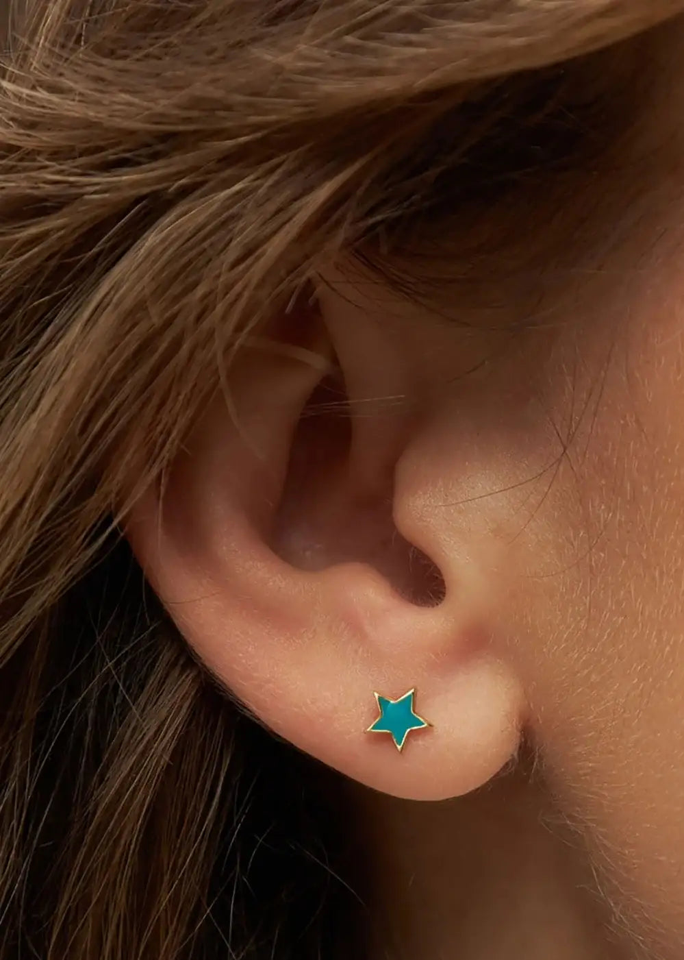 Petrol blue star-shaped gold plated ear stud on pierced ear