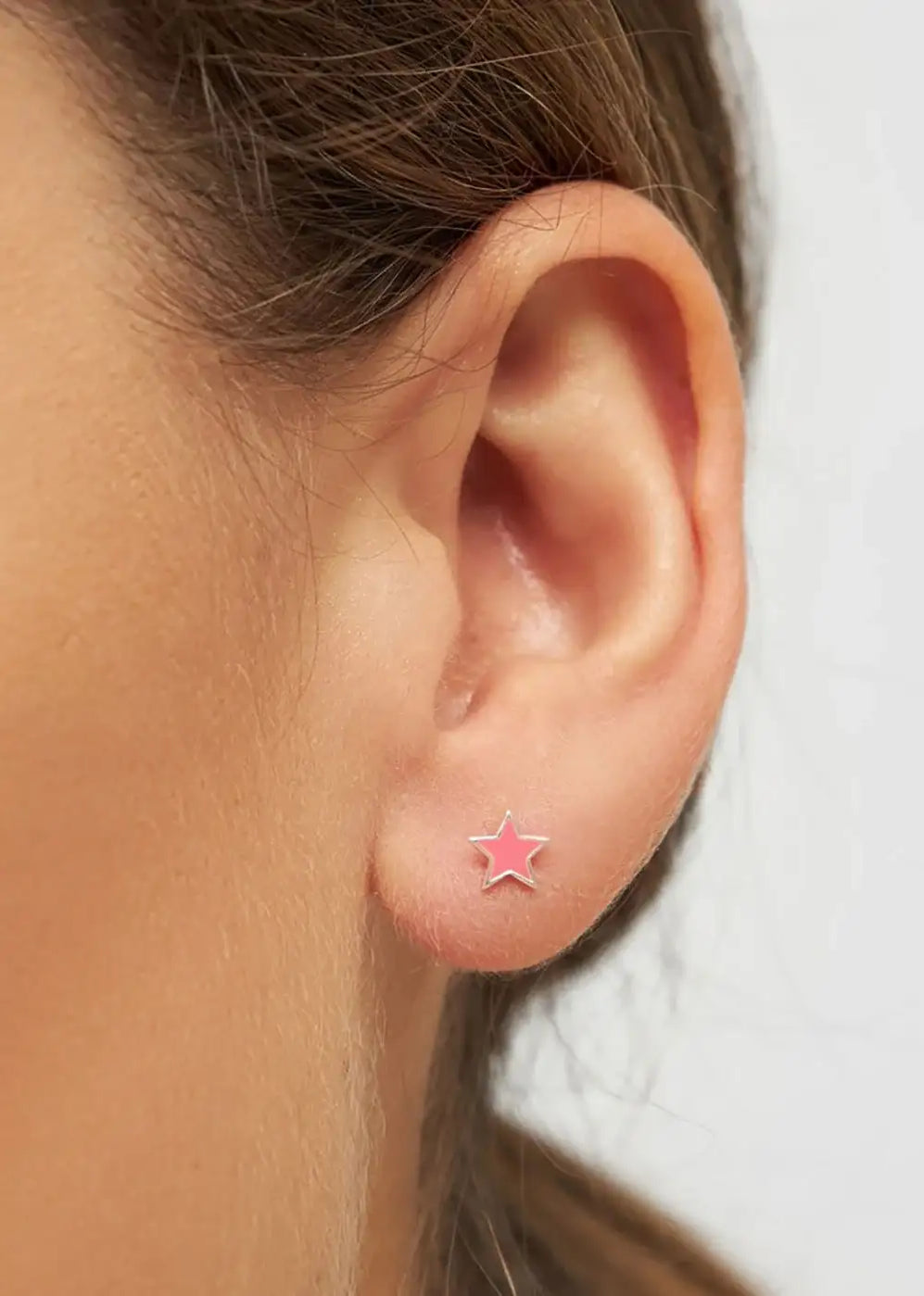 Close-up of ear wearing pink star silver stud earring, minimalist jewelry