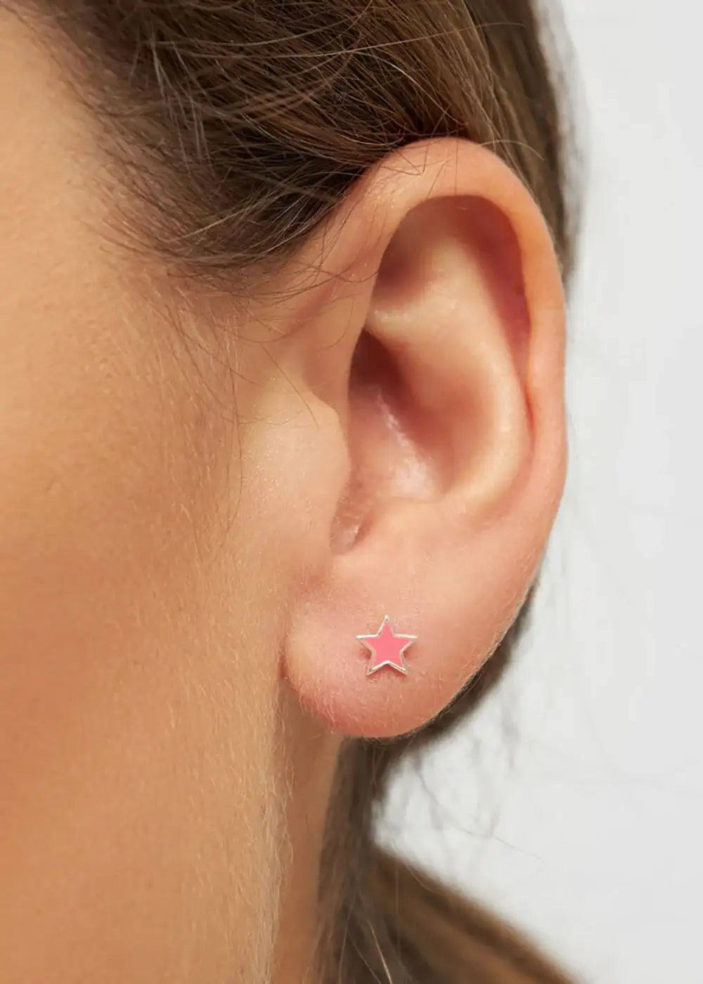 Close-up of ear wearing pink star silver stud earring, minimalist jewelry