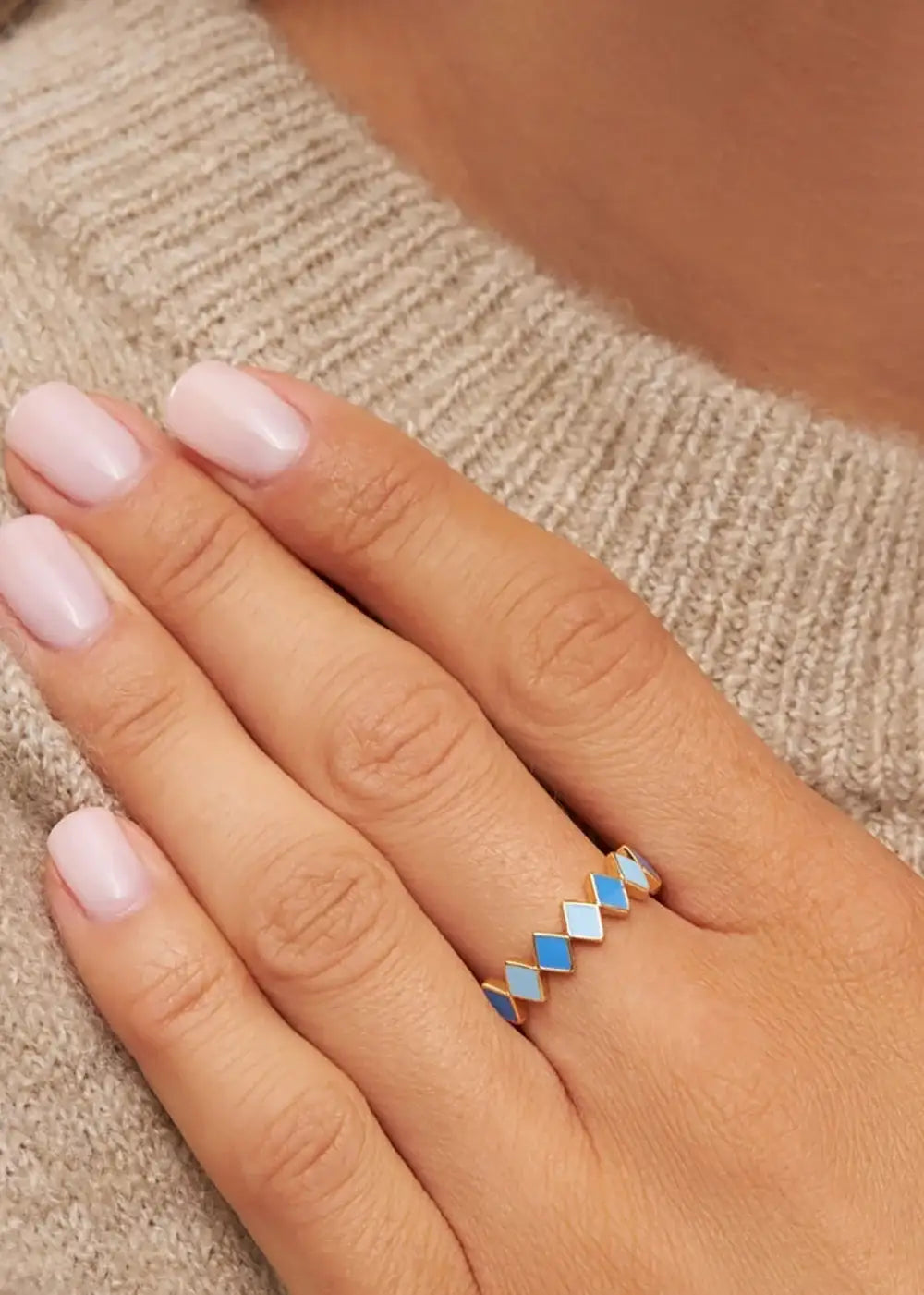 Gold plated geometric ring with blue and white enamel, worn on a hand with light pink nails